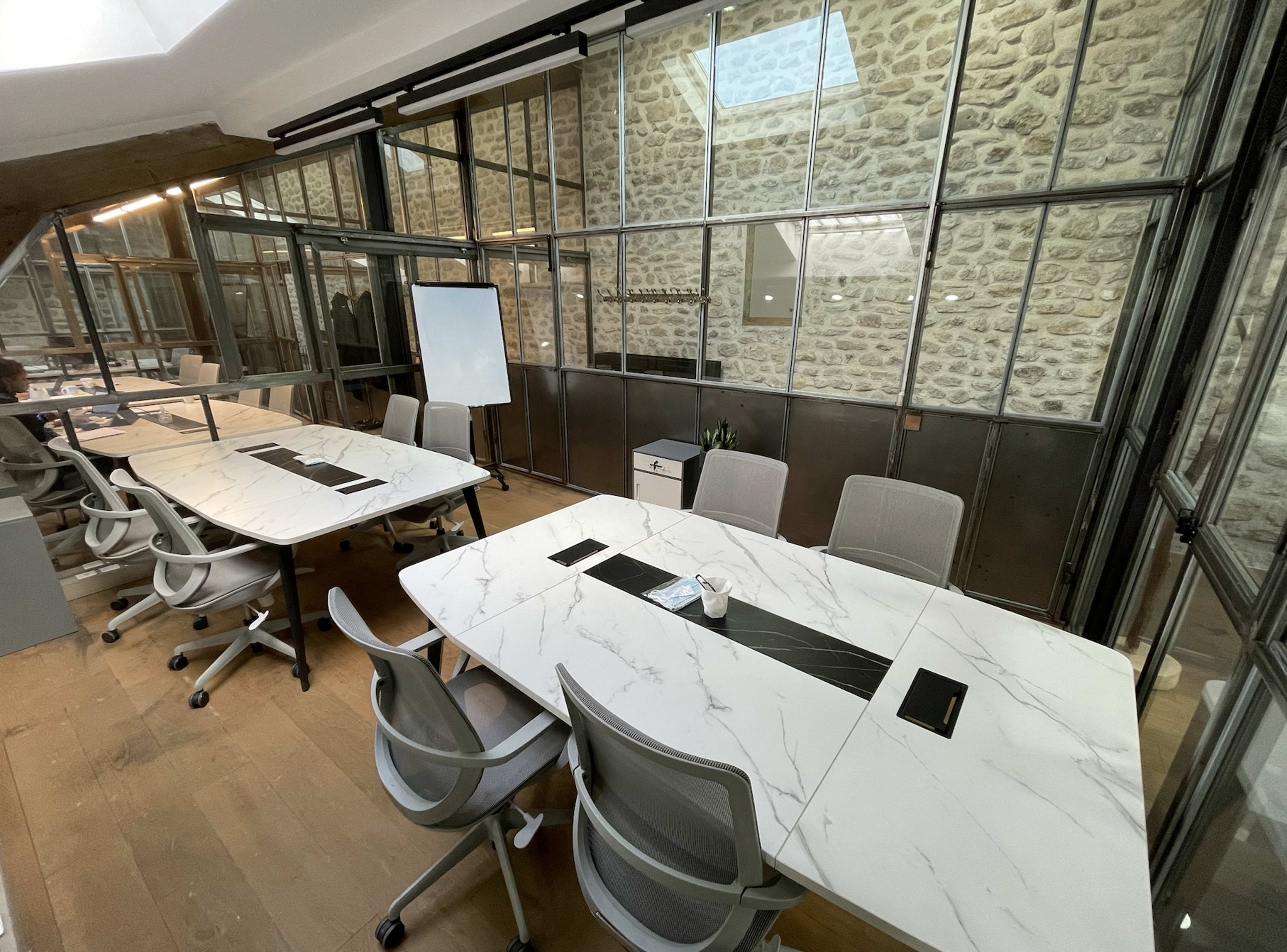 A modern office space featuring glass-walled meeting rooms with marble-topped tables and ergonomic chairs.