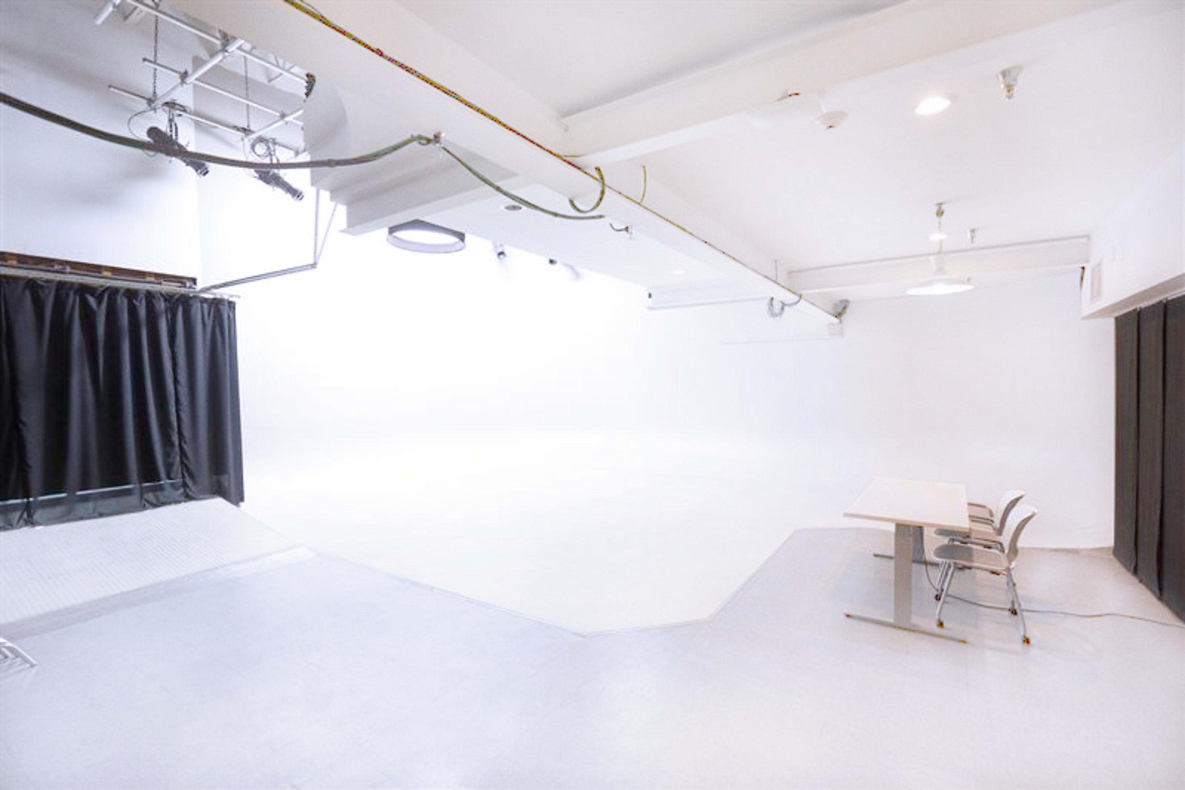 A spacious, well-lit studio with a white backdrop, a table, and a chair on a light-colored floor.