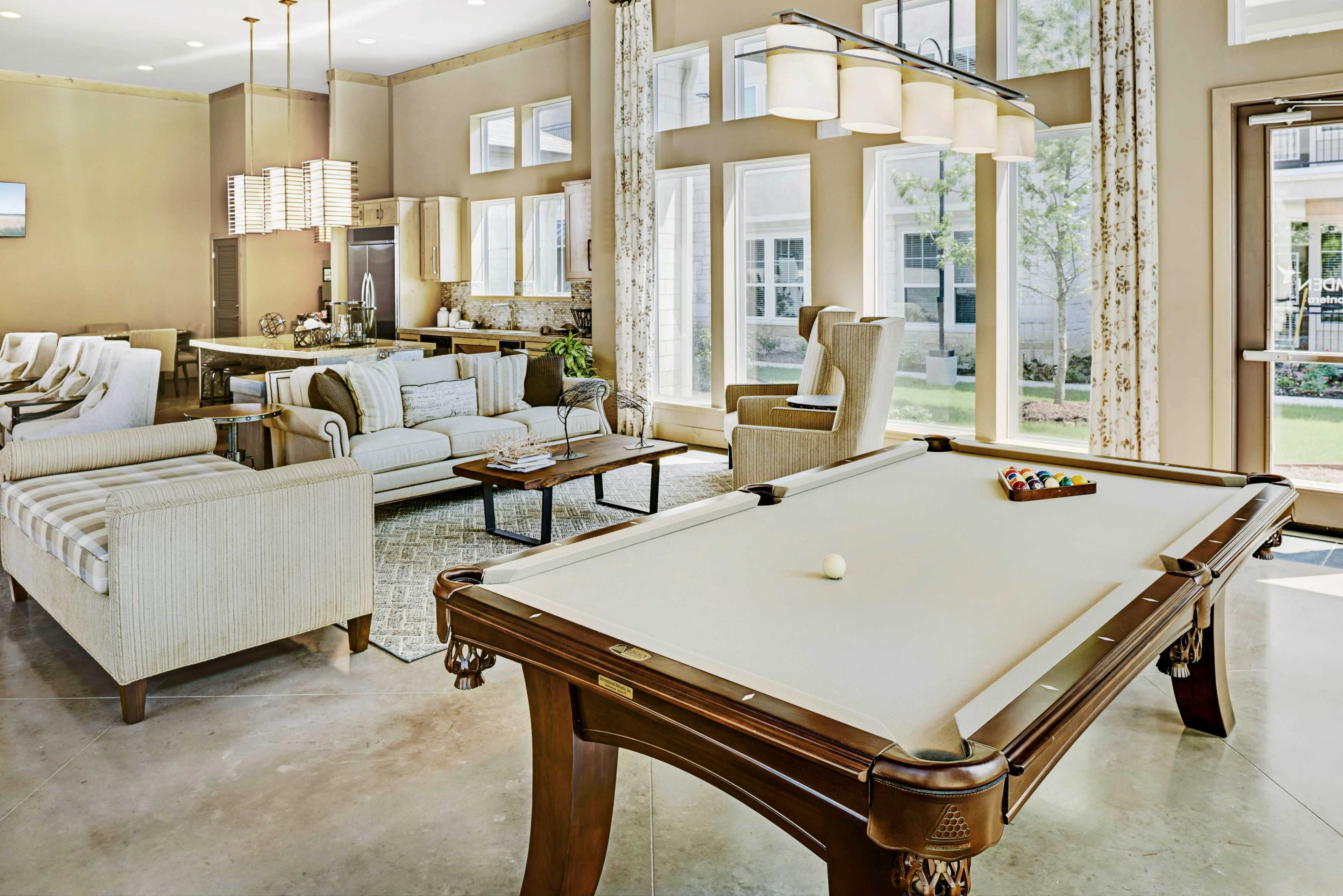 A spacious living area with a billiards table, comfortable seating, and large windows allowing natural light to fill the room.