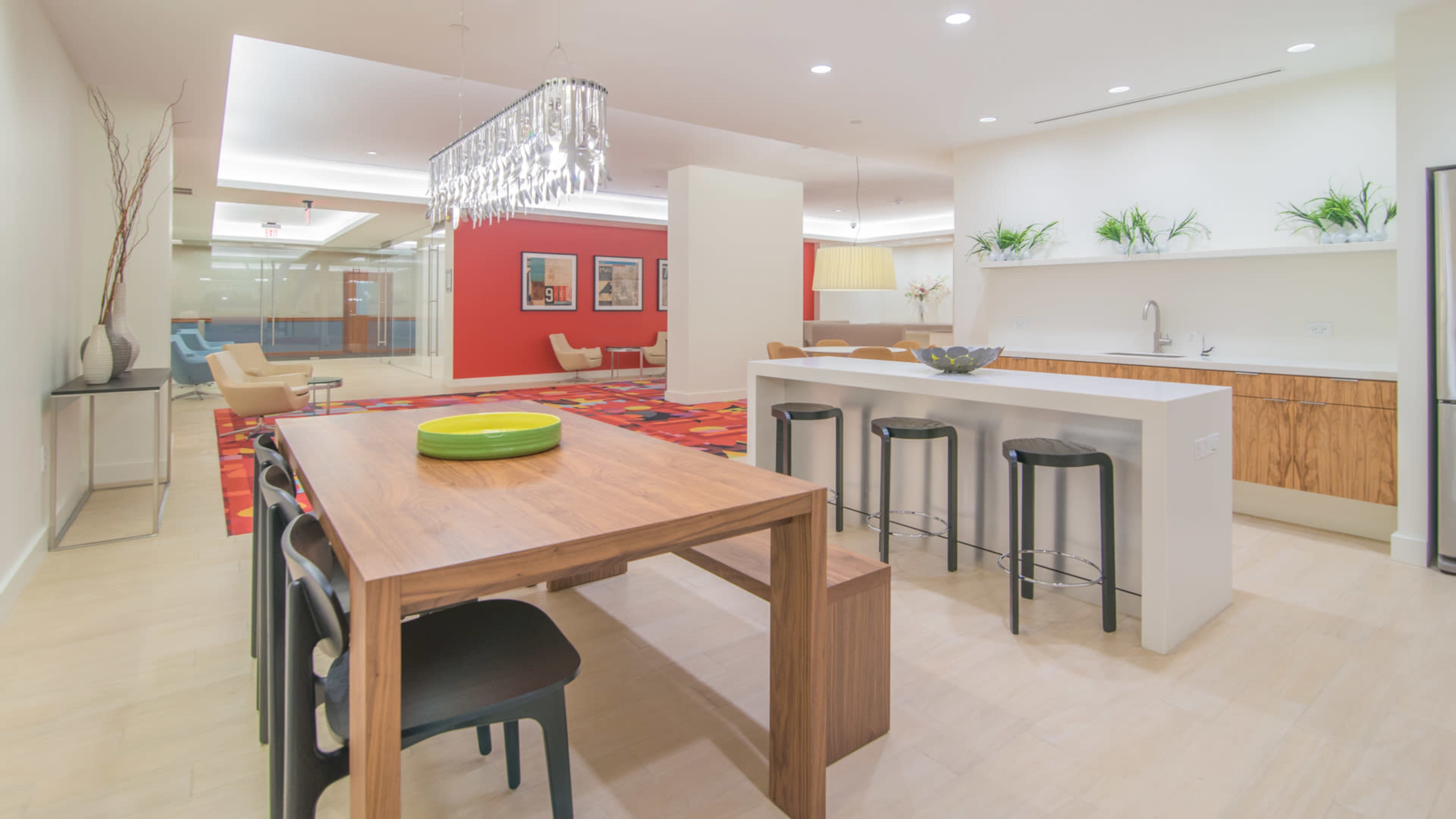 A modern kitchen and dining area features a wooden table with black chairs, a sleek island with a sink, and bright red accents on the walls.