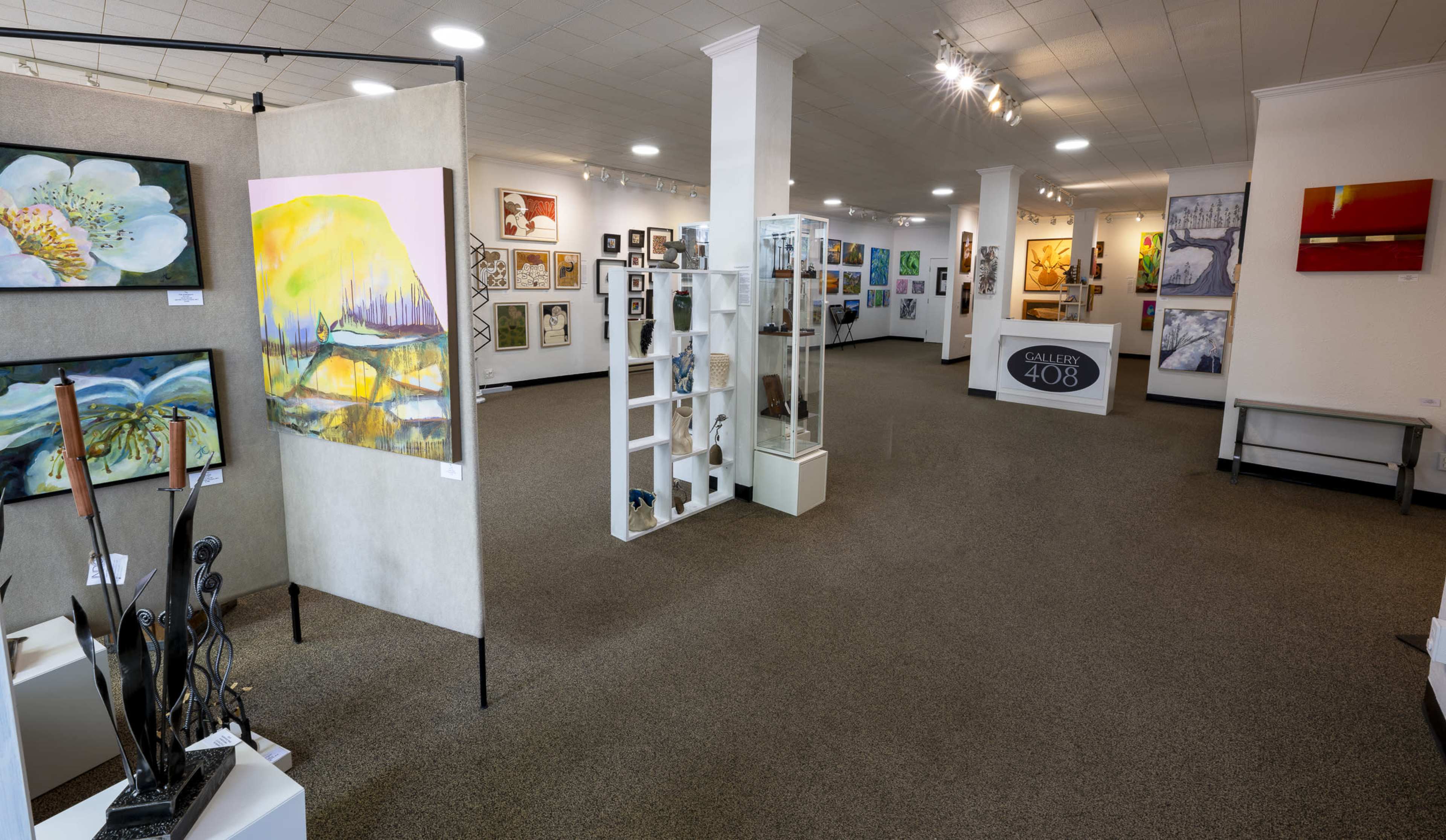 The image shows the interior of an art gallery featuring various artworks displayed on walls and stands.
