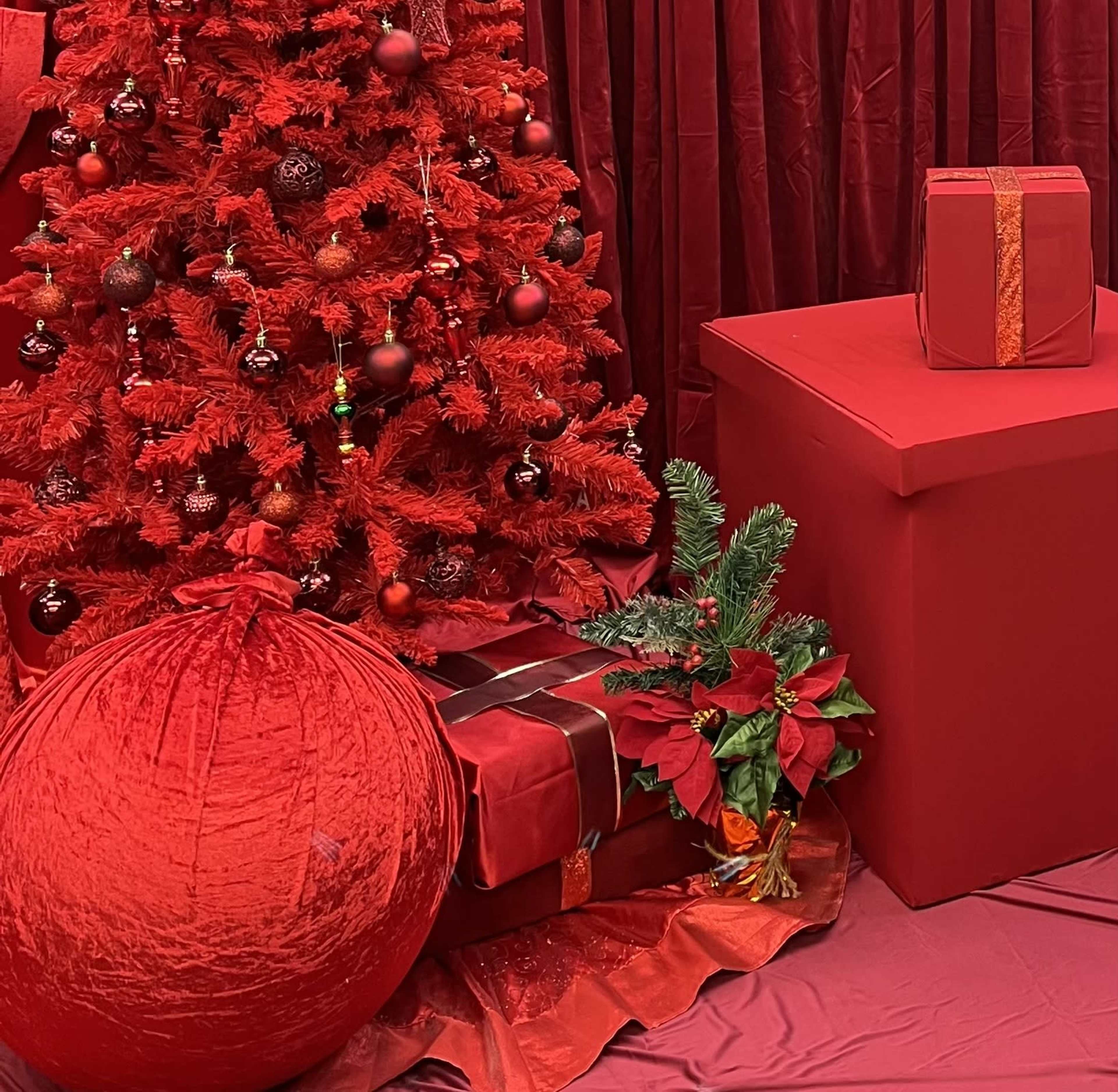 The scene features a red Christmas tree surrounded by red decorations, a large red gift box, and wrapped presents.
