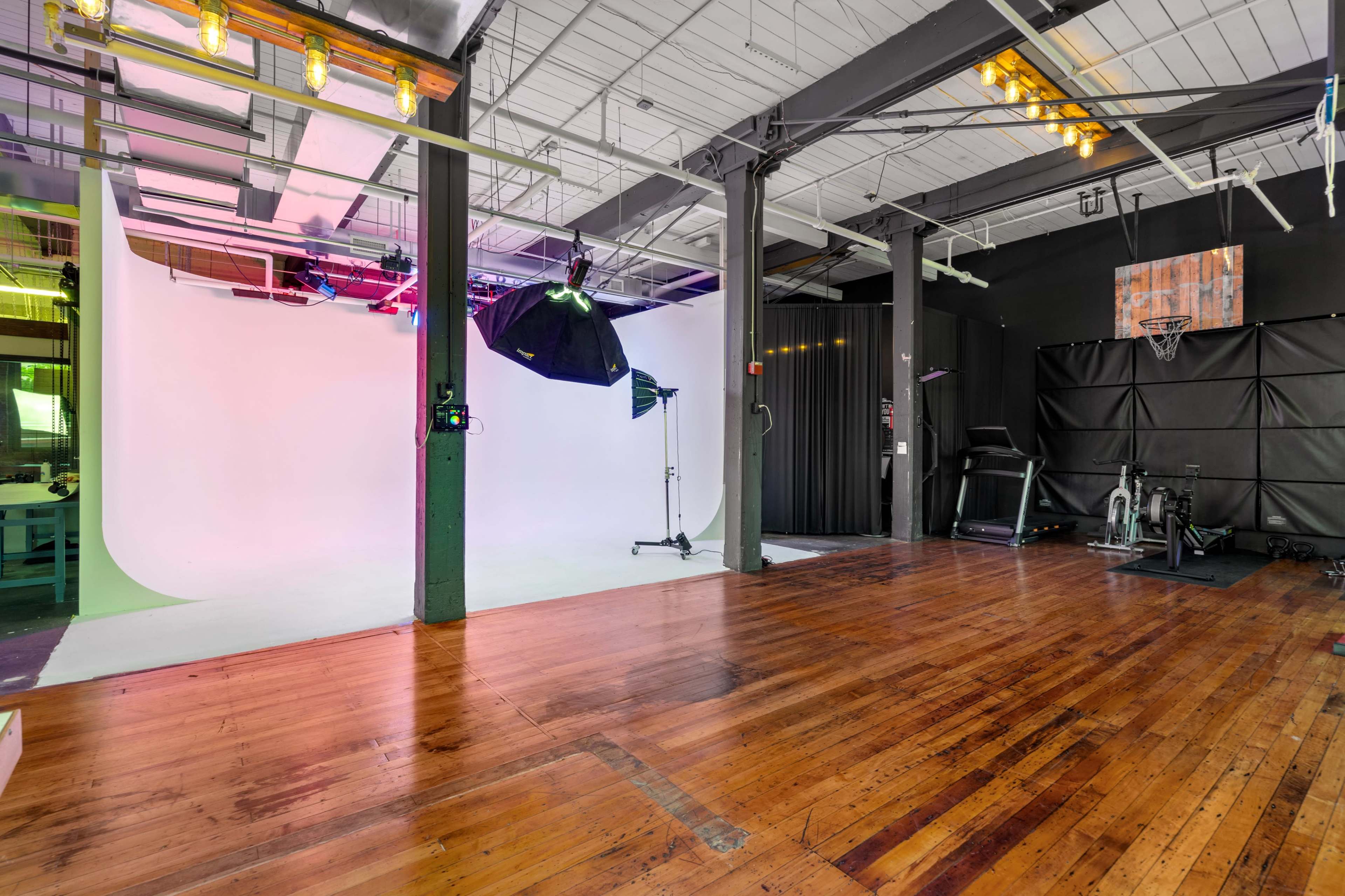 A spacious studio with a white backdrop, various lighting equipment, and a hardwood floor.