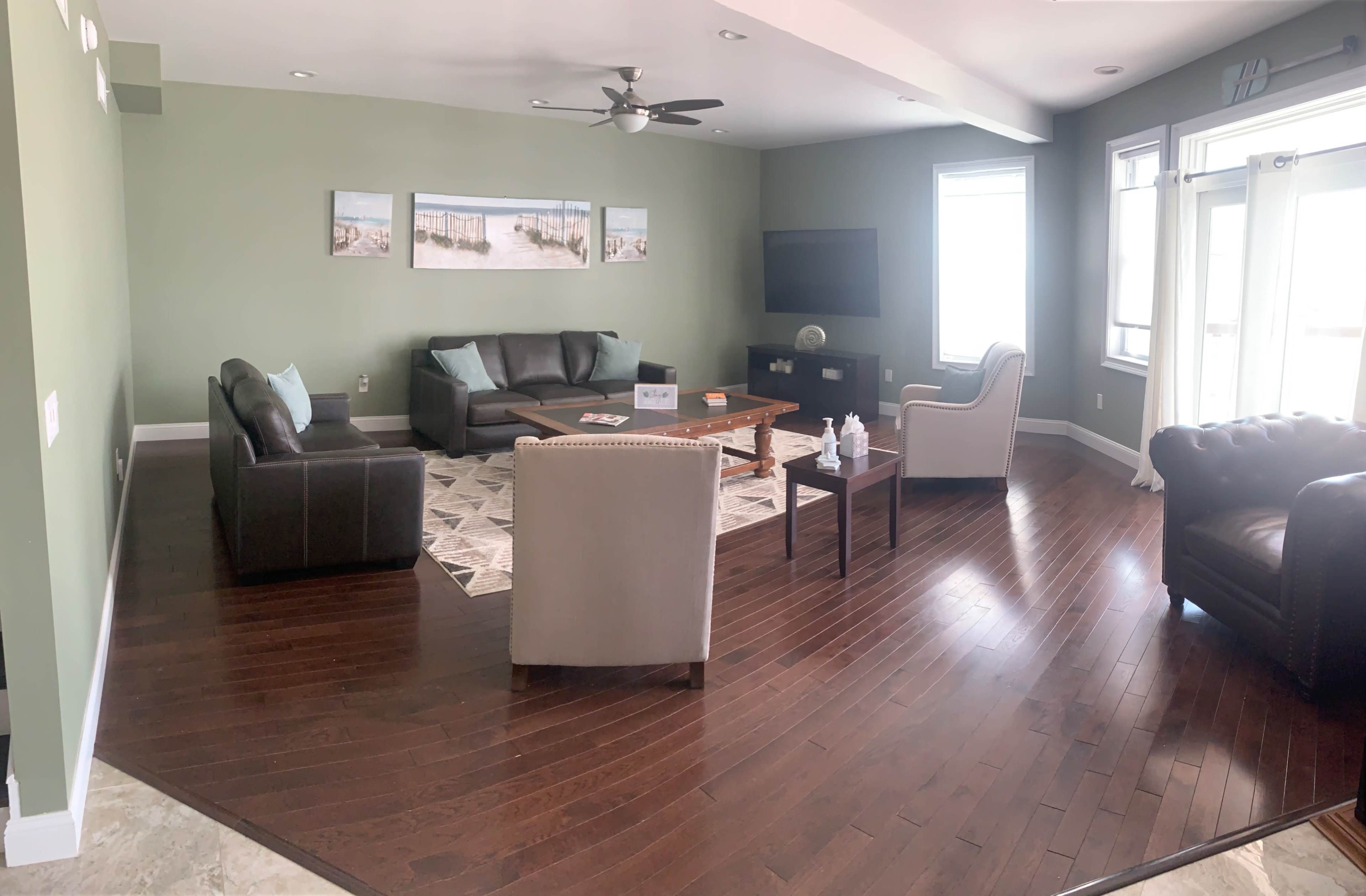 A spacious living room with dark hardwood flooring, modern furniture, and a large window letting in natural light.