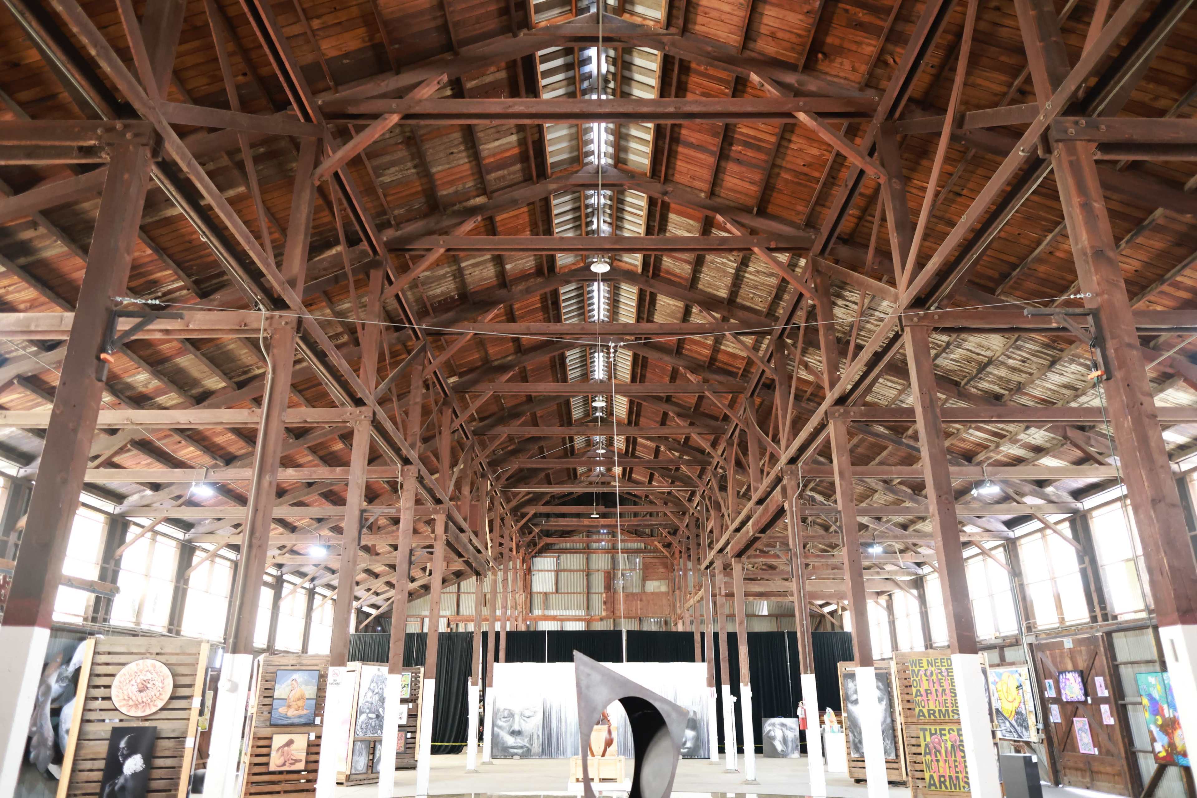 The image shows the interior of a large wooden barn with exposed beams and various artworks displayed on the walls.