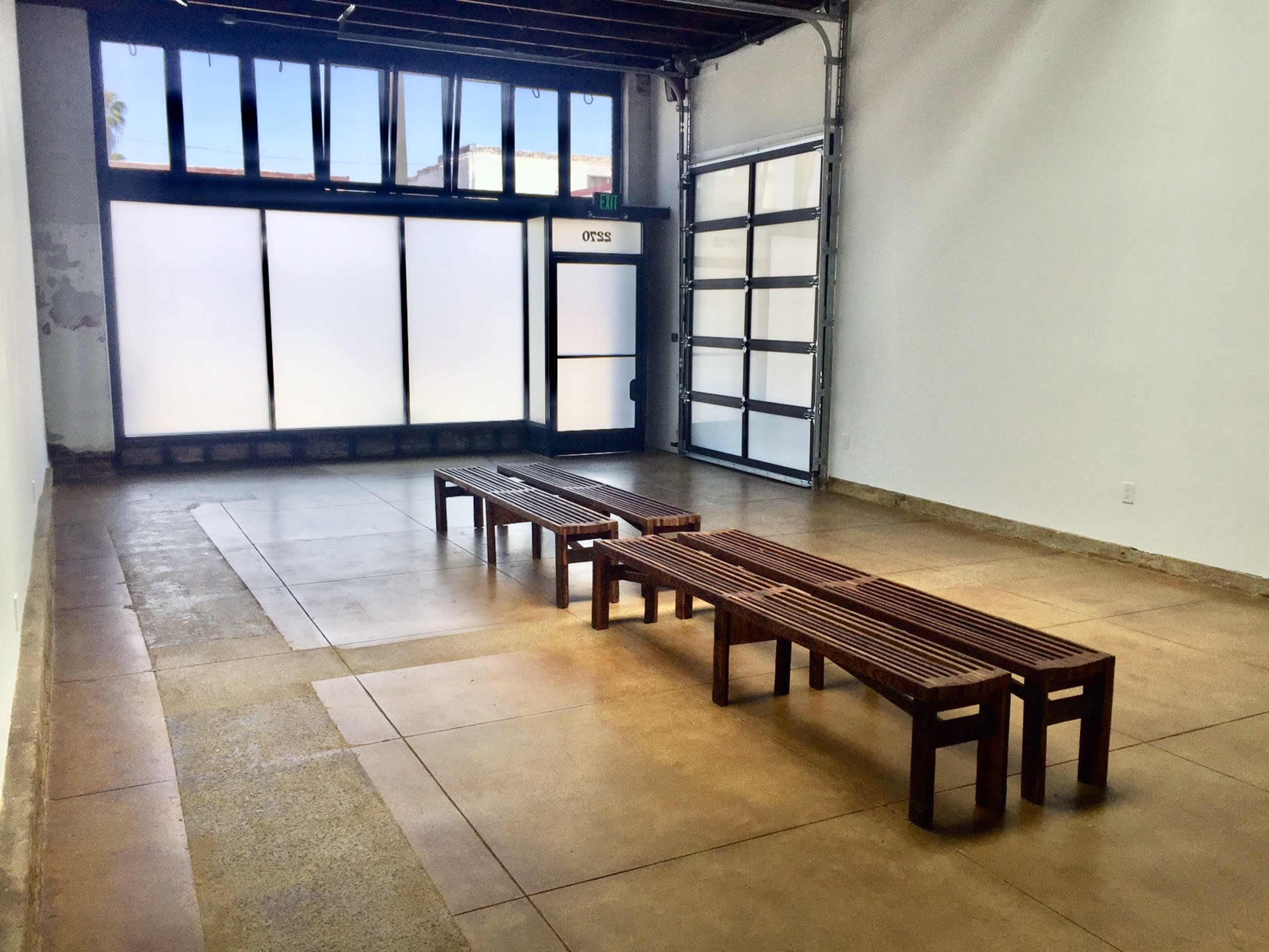 An empty room with concrete flooring and two long wooden benches placed parallel to a large window.