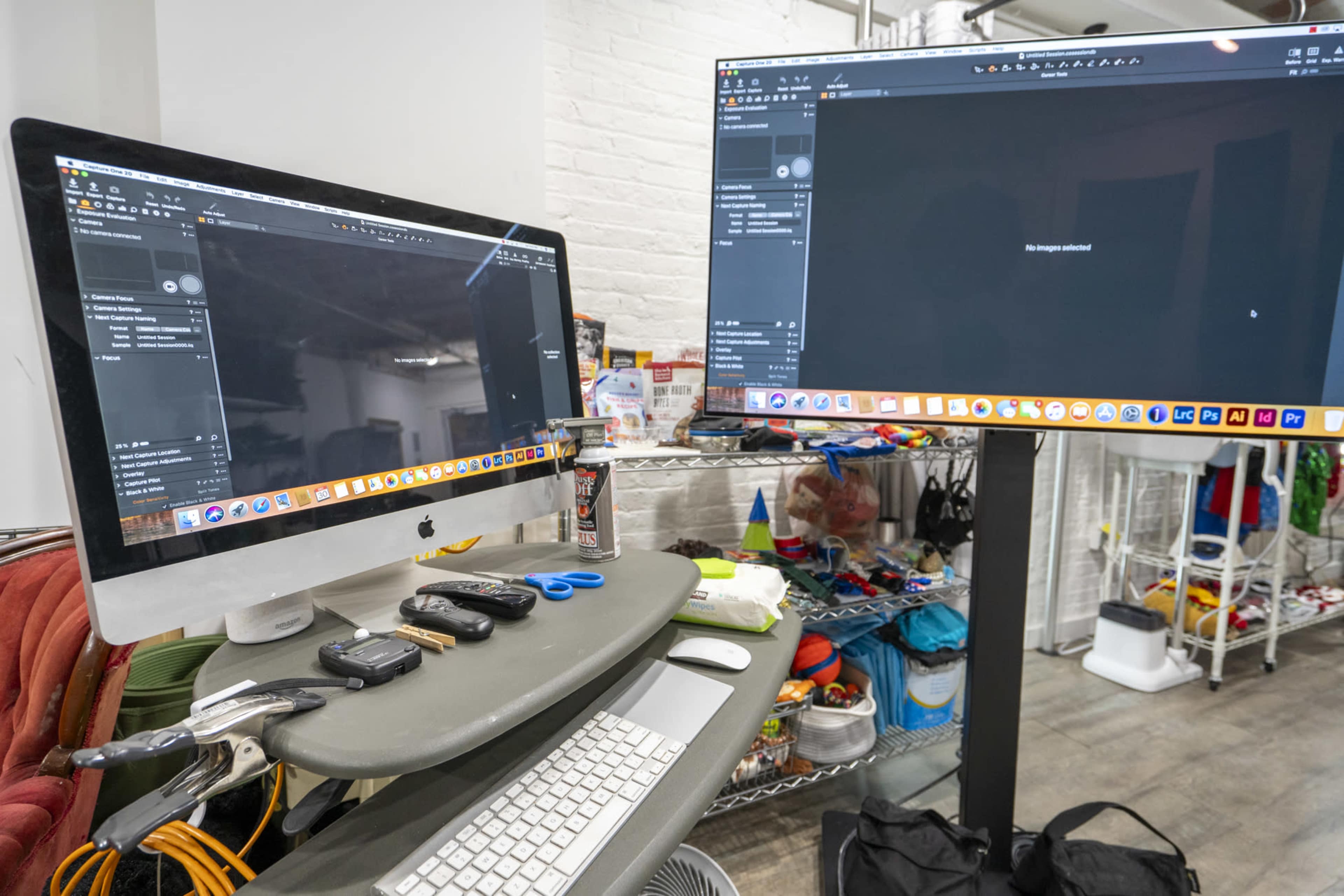 A workspace with an iMac and a large external monitor displaying dark screens, surrounded by various tools and items on a table.