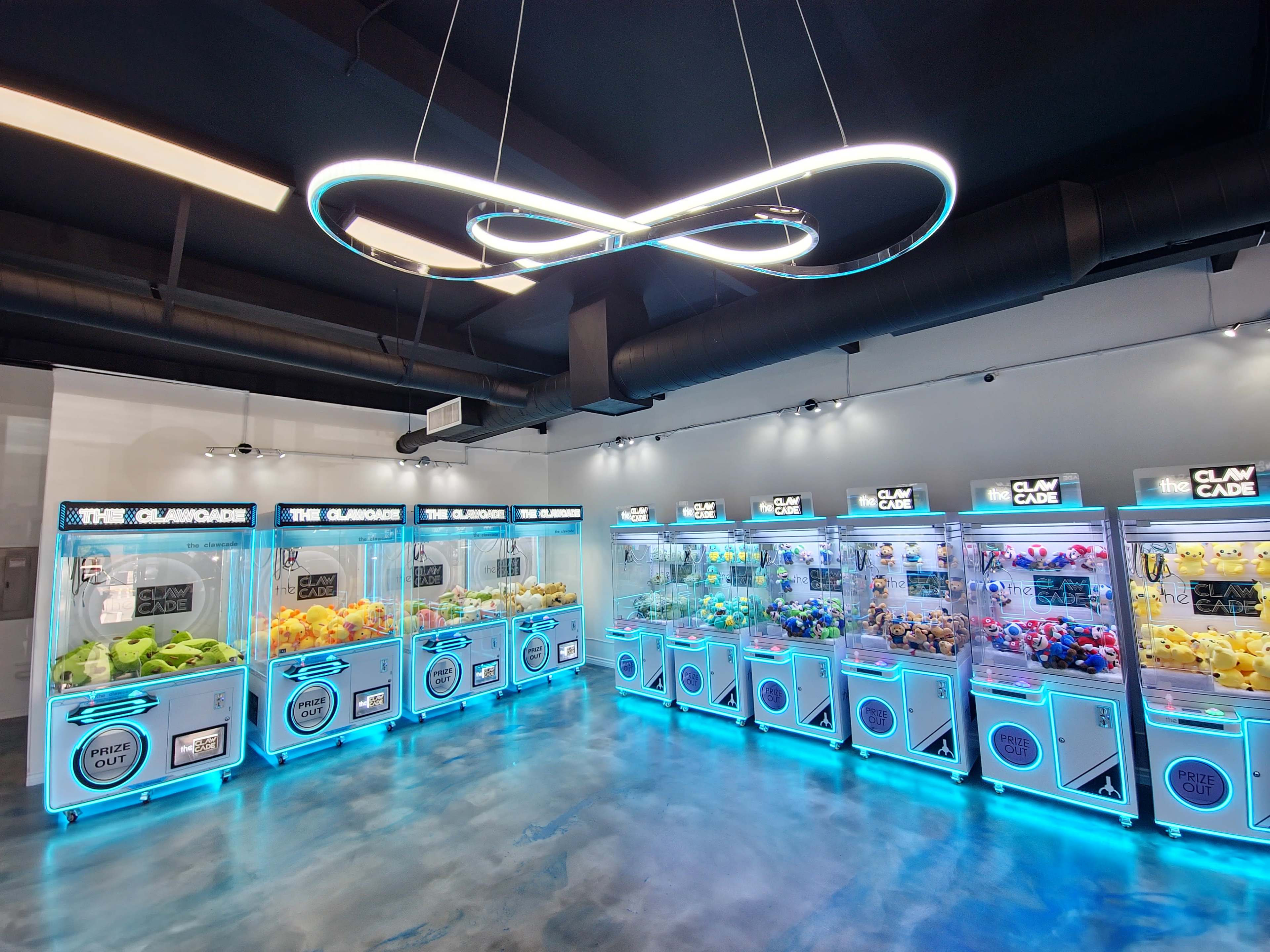 The image shows an arcade room filled with claw machine games, each featuring brightly colored plush toys and illuminated with blue LED lights.