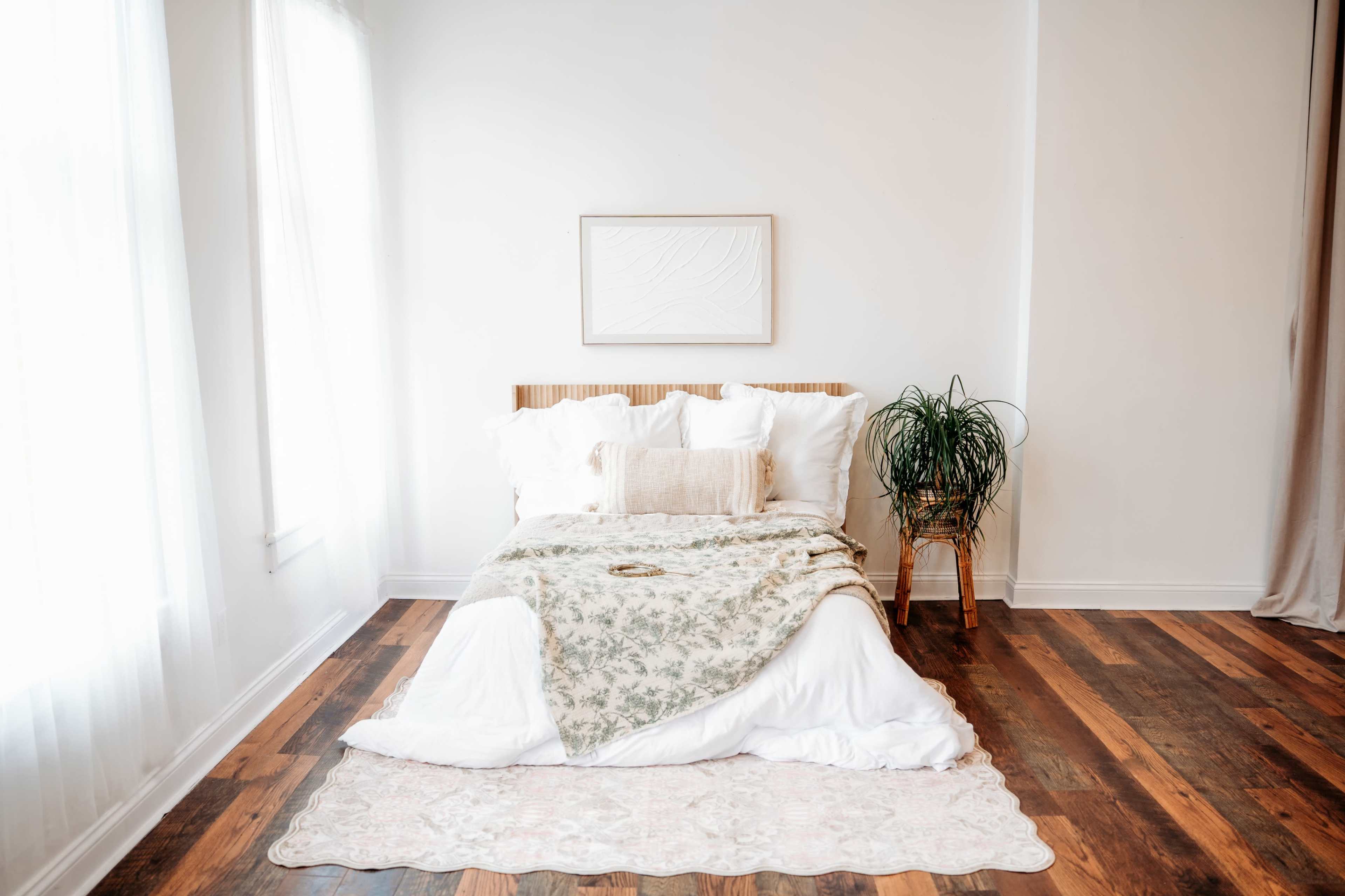 A neatly made bed with a decorative blanket and pillows is positioned in a spacious, bright room with wooden floors.