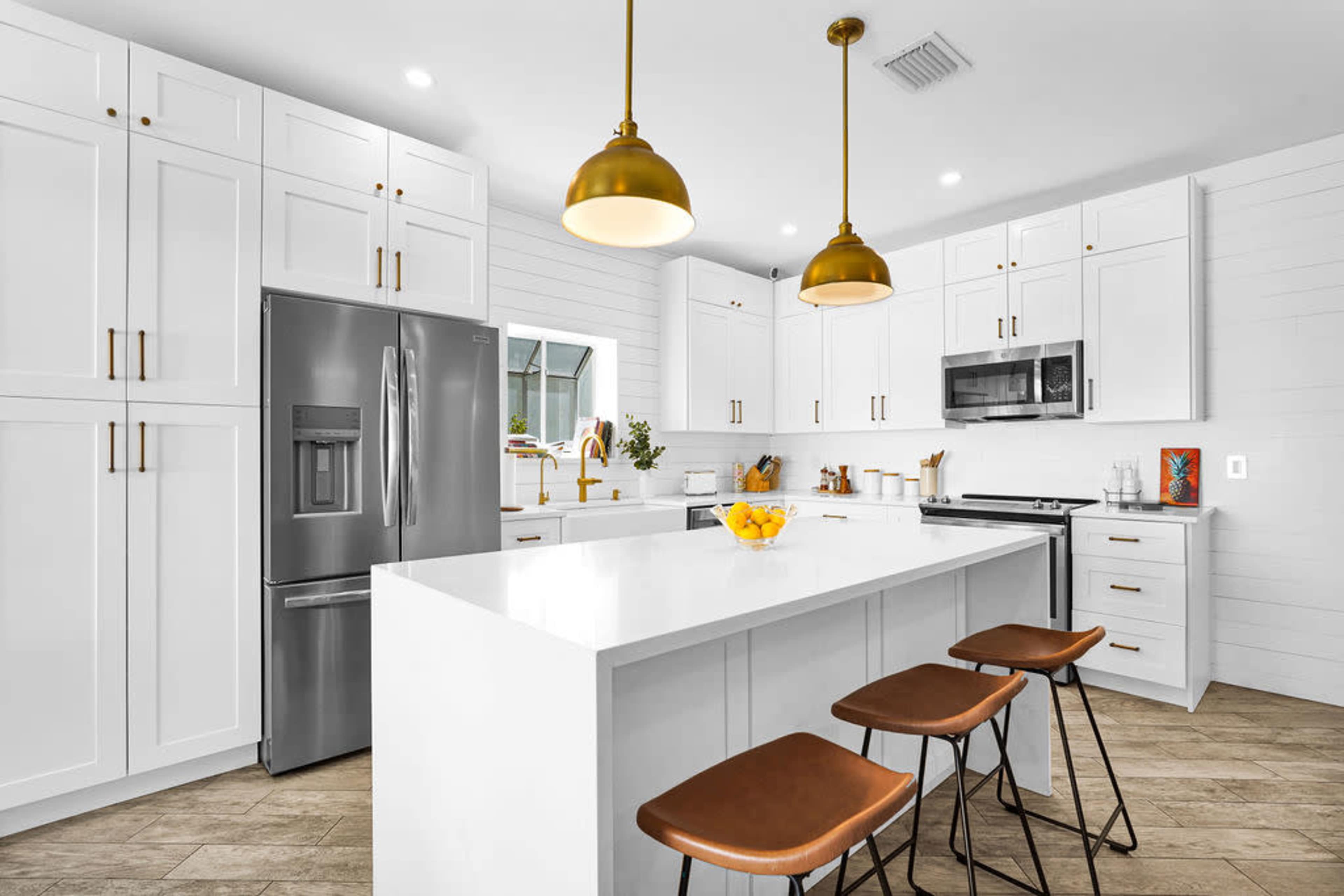 A modern kitchen features white cabinetry, stainless steel appliances, and a large island with three bar stools.