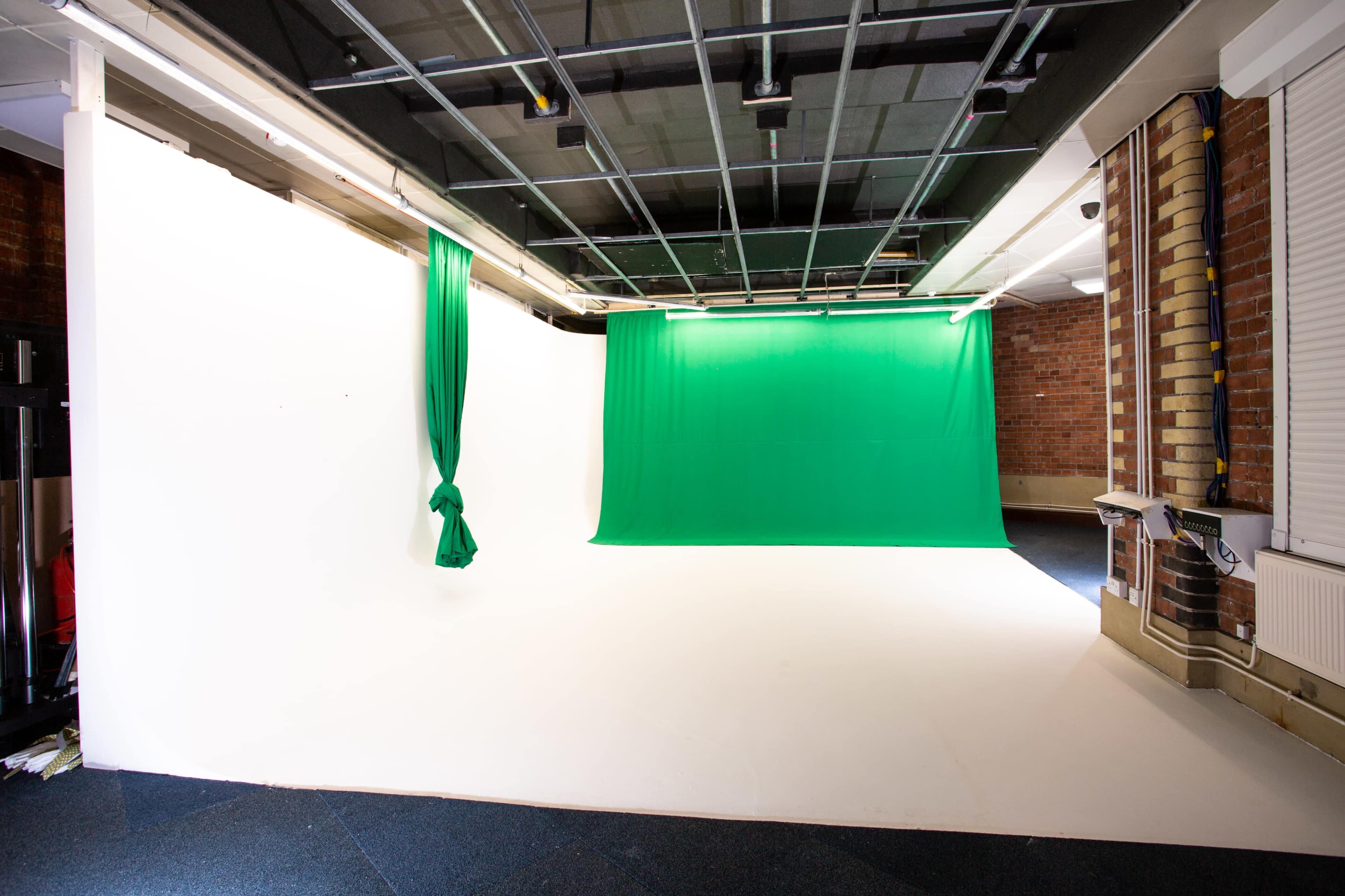 A studio space with a green screen backdrop and a white wall, featuring a clean, empty floor.