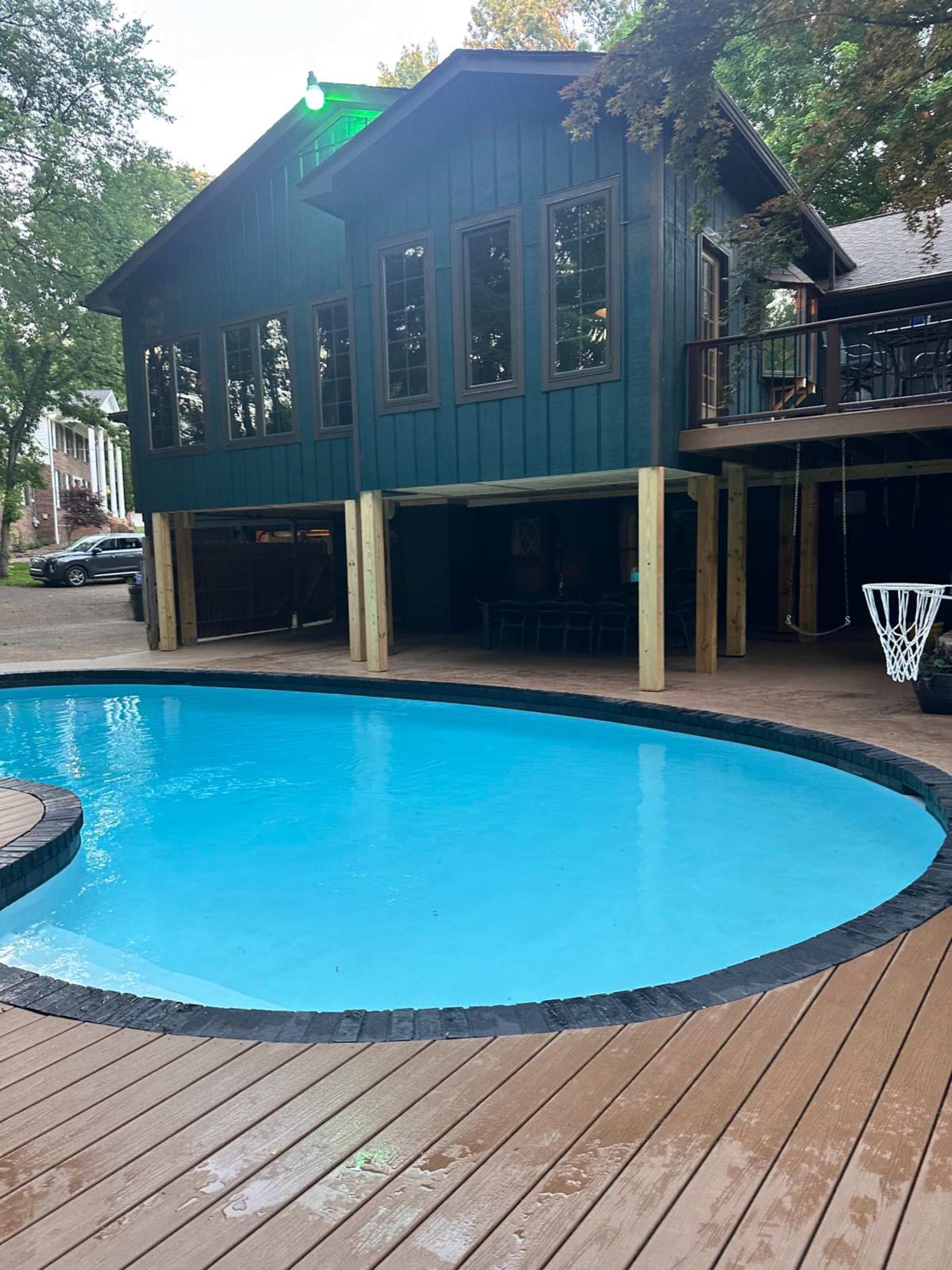 A blue swimming pool is situated in front of a two-story building with large windows and a wooden deck.