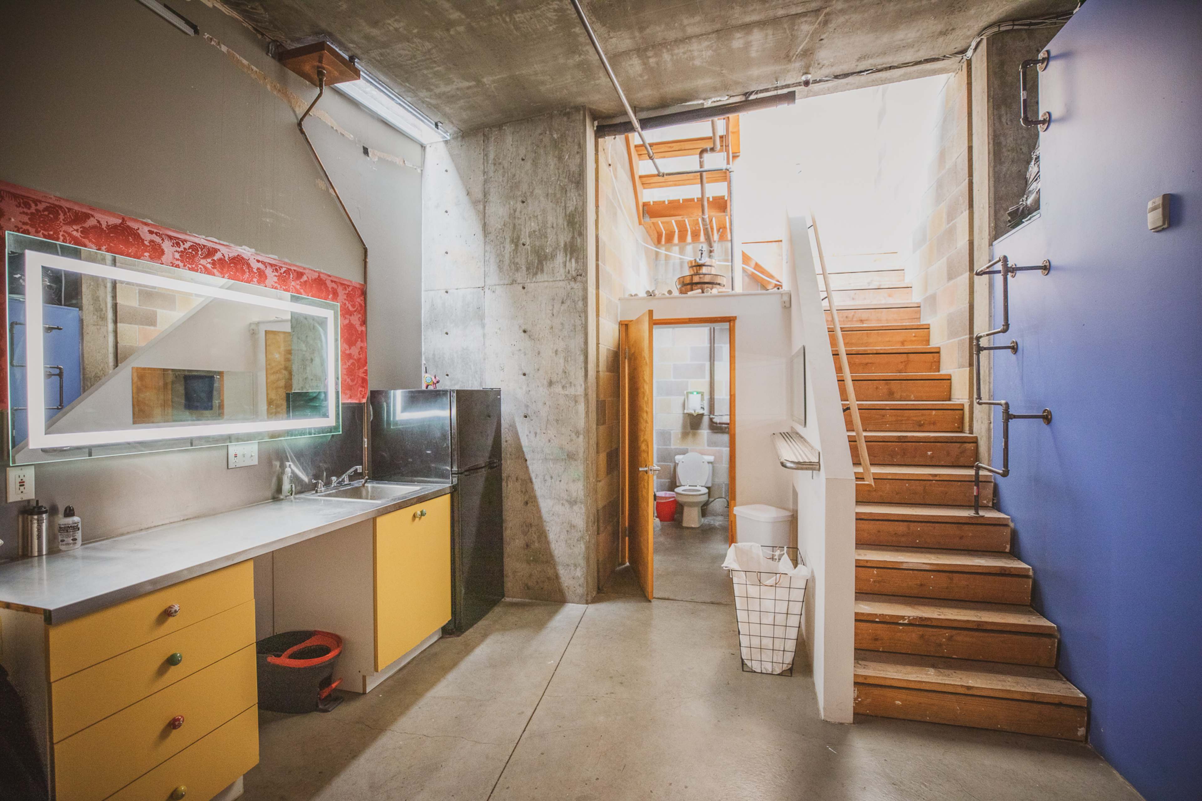 The image shows a modern interior space featuring a kitchen area with yellow cabinets and a staircase leading to an upper level.