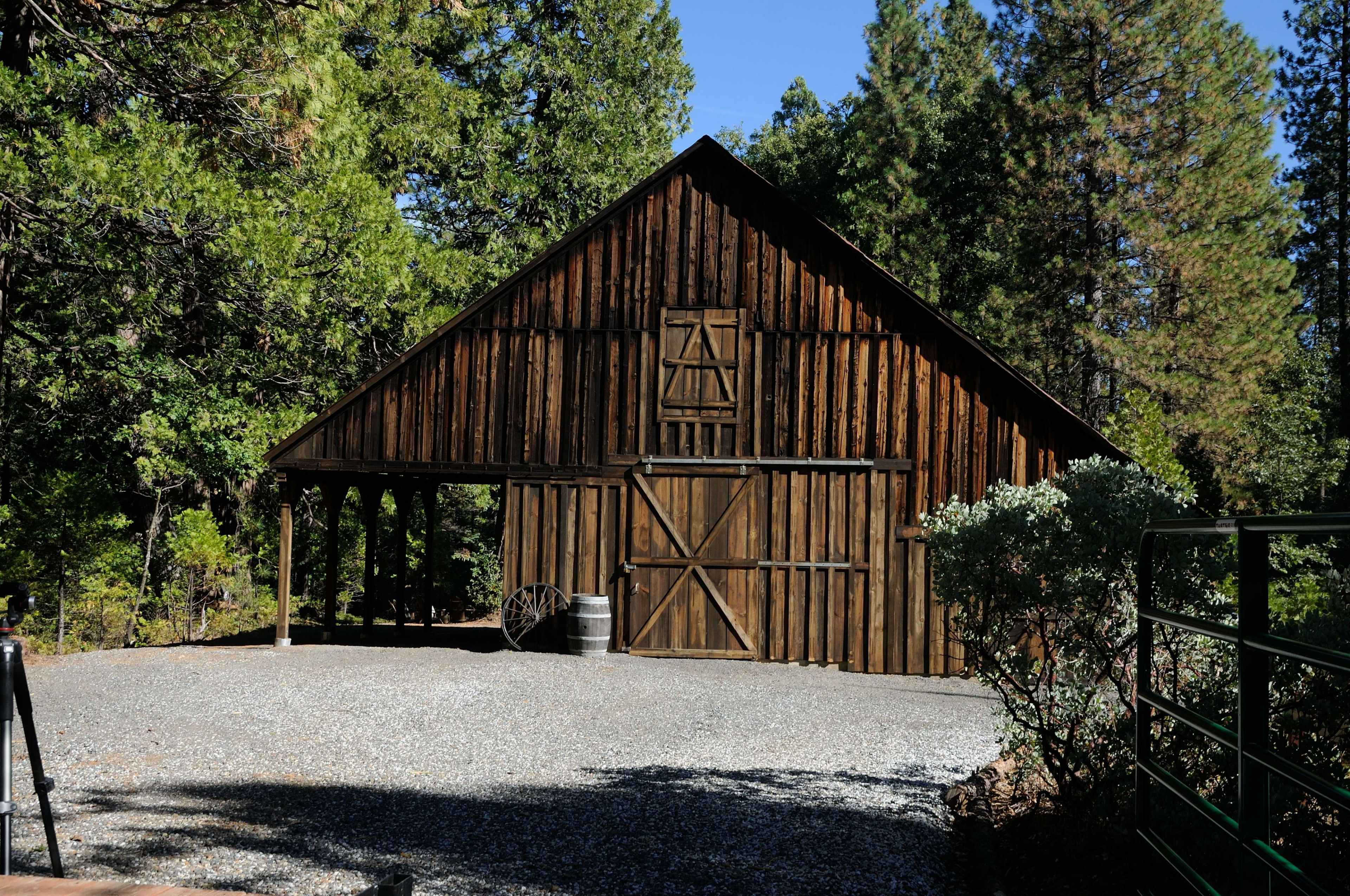 A wooden barn stands in a forested area, with a gravel path leading up to it.