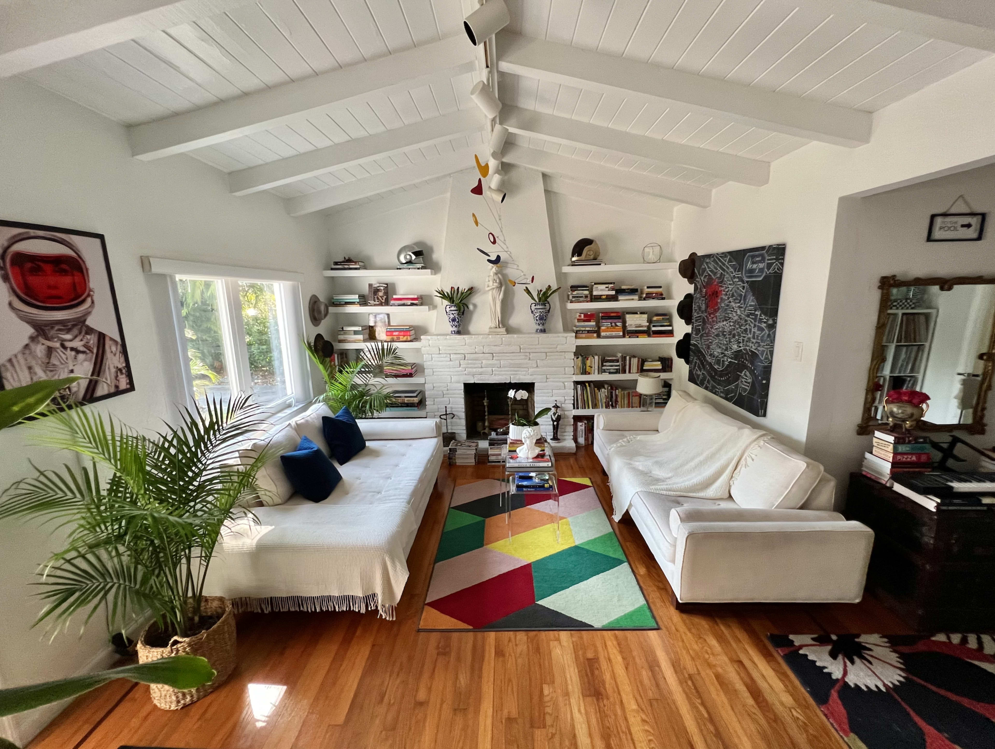A cozy living room features two couches, a colorful area rug, a bookshelf filled with books, and a decorative fireplace.