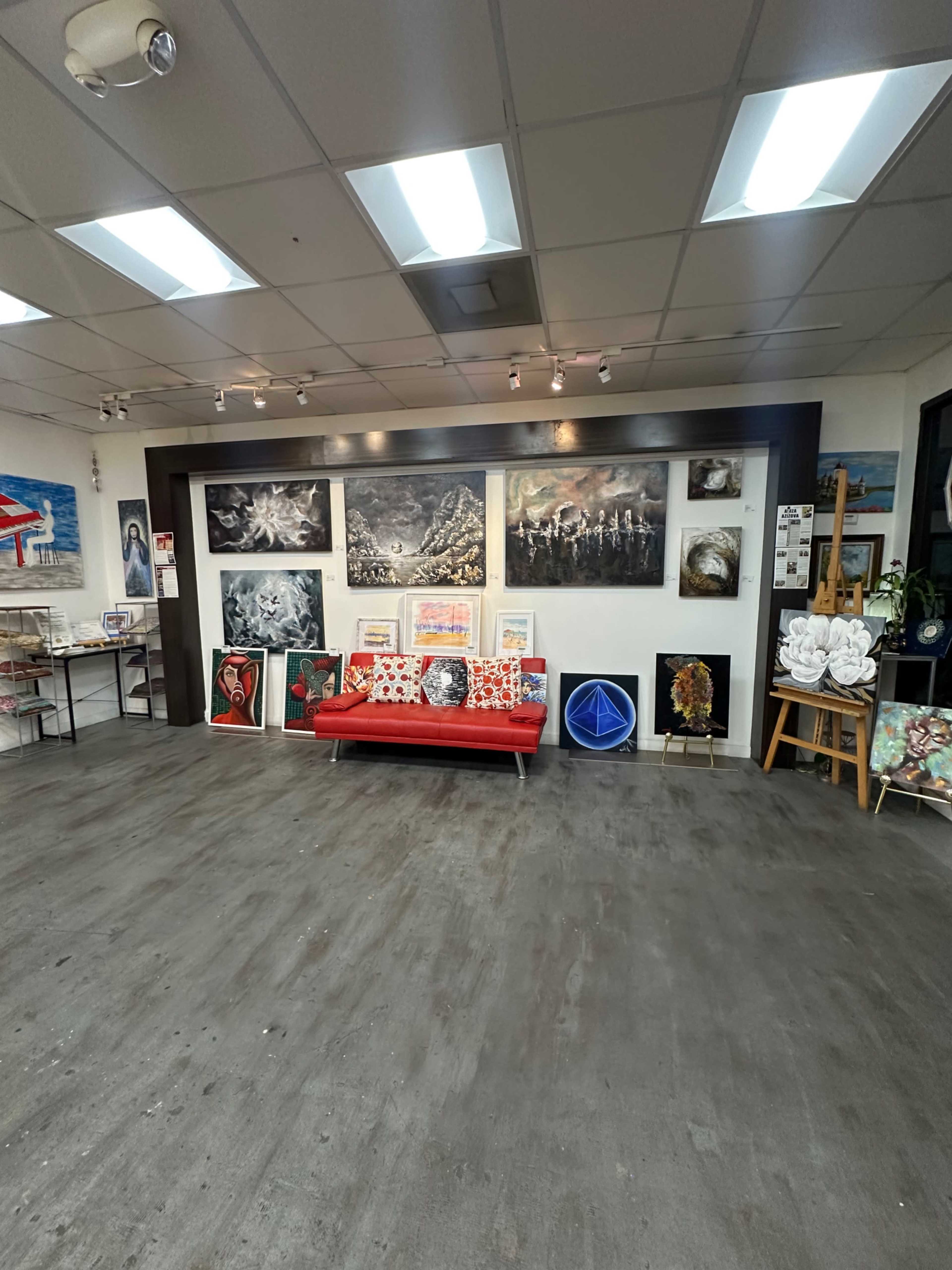 The image shows an art gallery featuring a red couch, various artworks on the walls, and displays of pictures and paintings throughout the space.