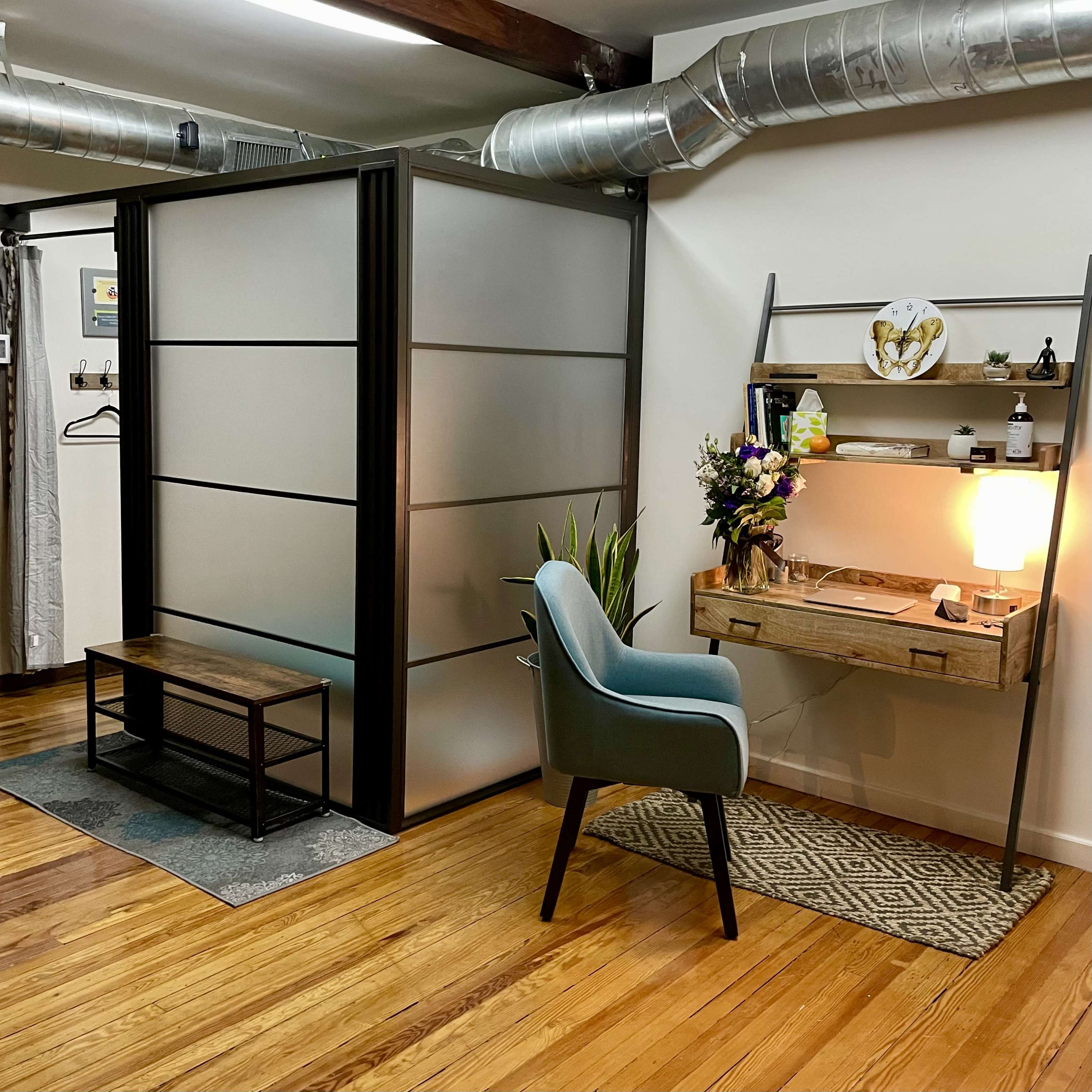 The image shows a modern office space featuring a partitioned area with a desk, chair, and decorative elements against a backdrop of wooden flooring and industrial-style ductwork.