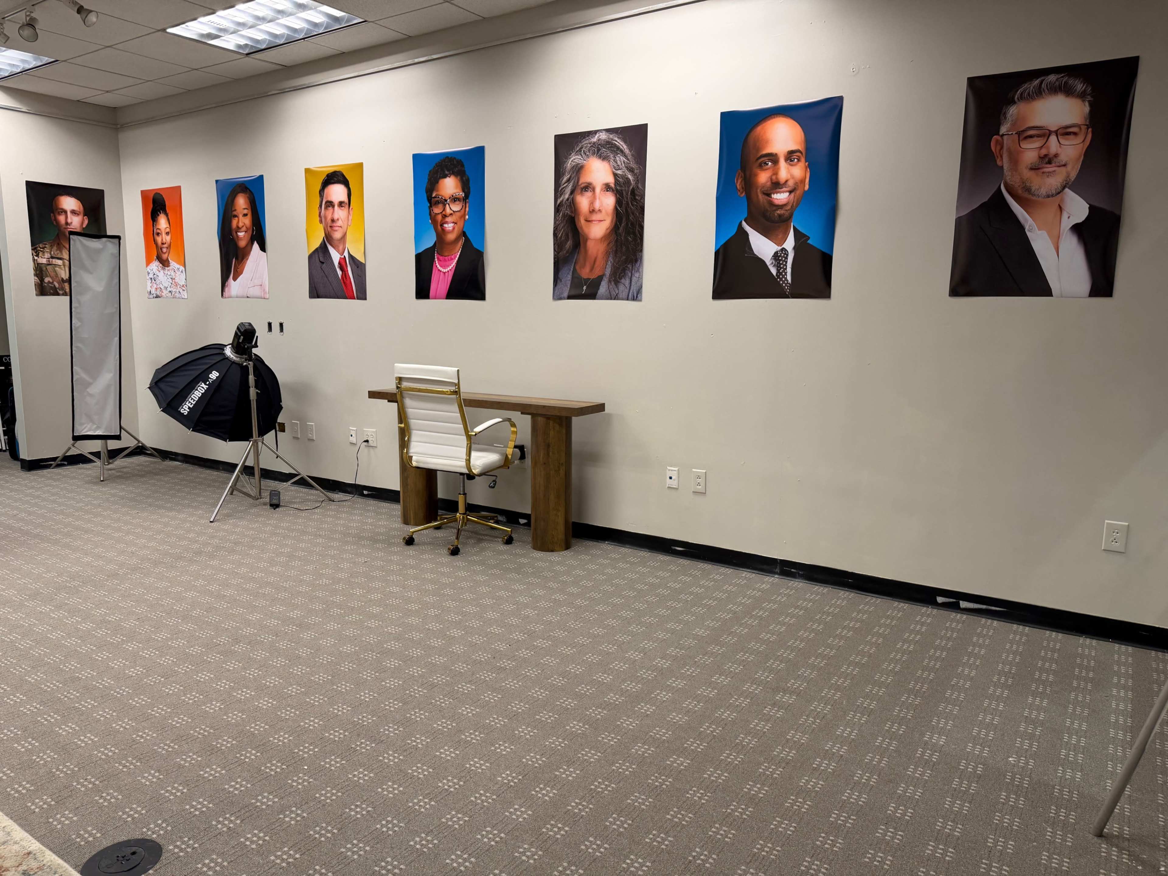 The image shows a room with a patterned carpet and a desk, featuring large portraits of various individuals mounted on the wall.