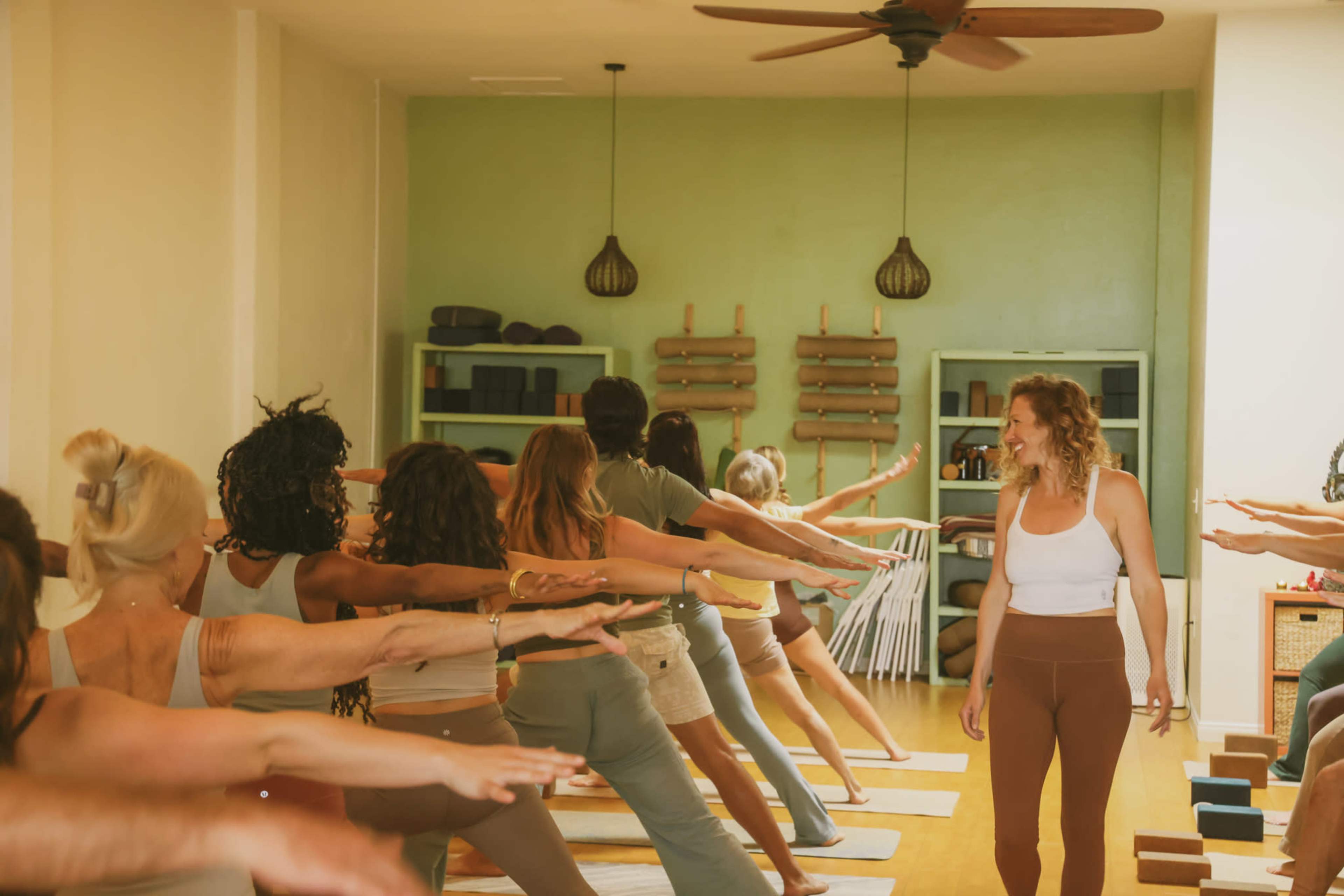 A yoga class is being conducted in a serene studio with participants engaged in a pose while facing the instructor.