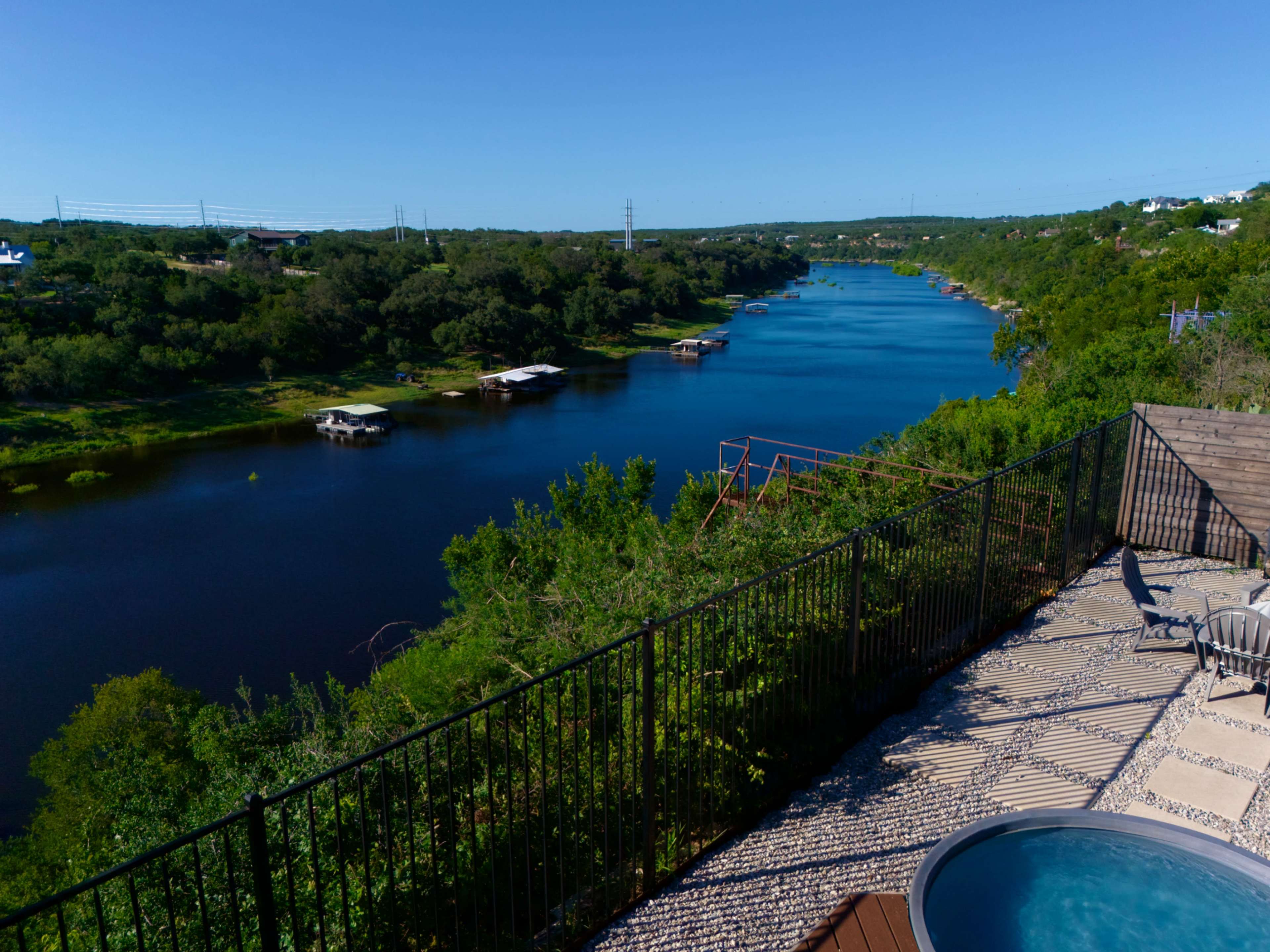 The image shows a tranquil river view lined with trees and boat docks, with a pool and patio area in the foreground.