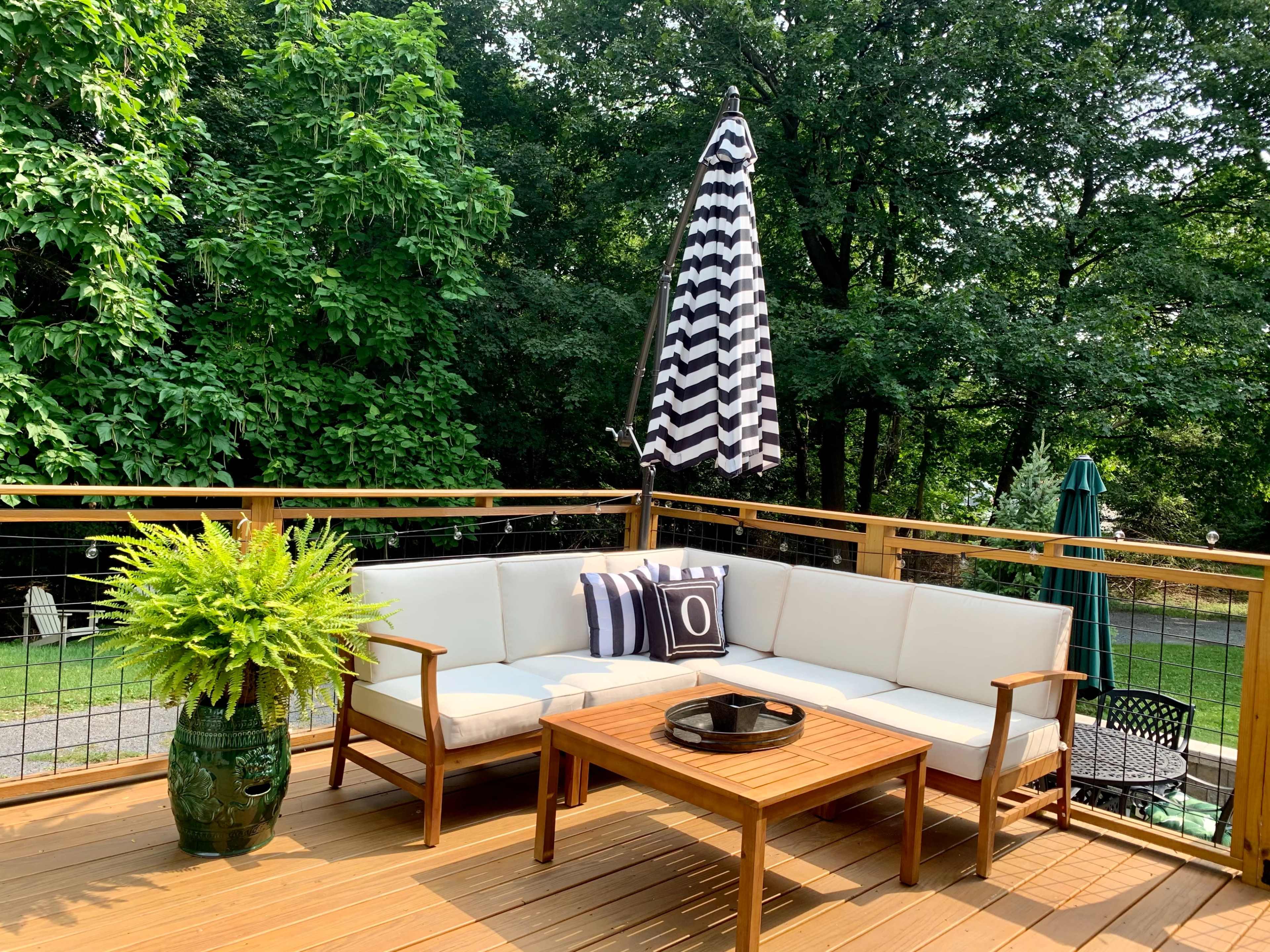 A patio seating area features a sectional sofa with a coffee table, surrounded by greenery and a large striped umbrella.