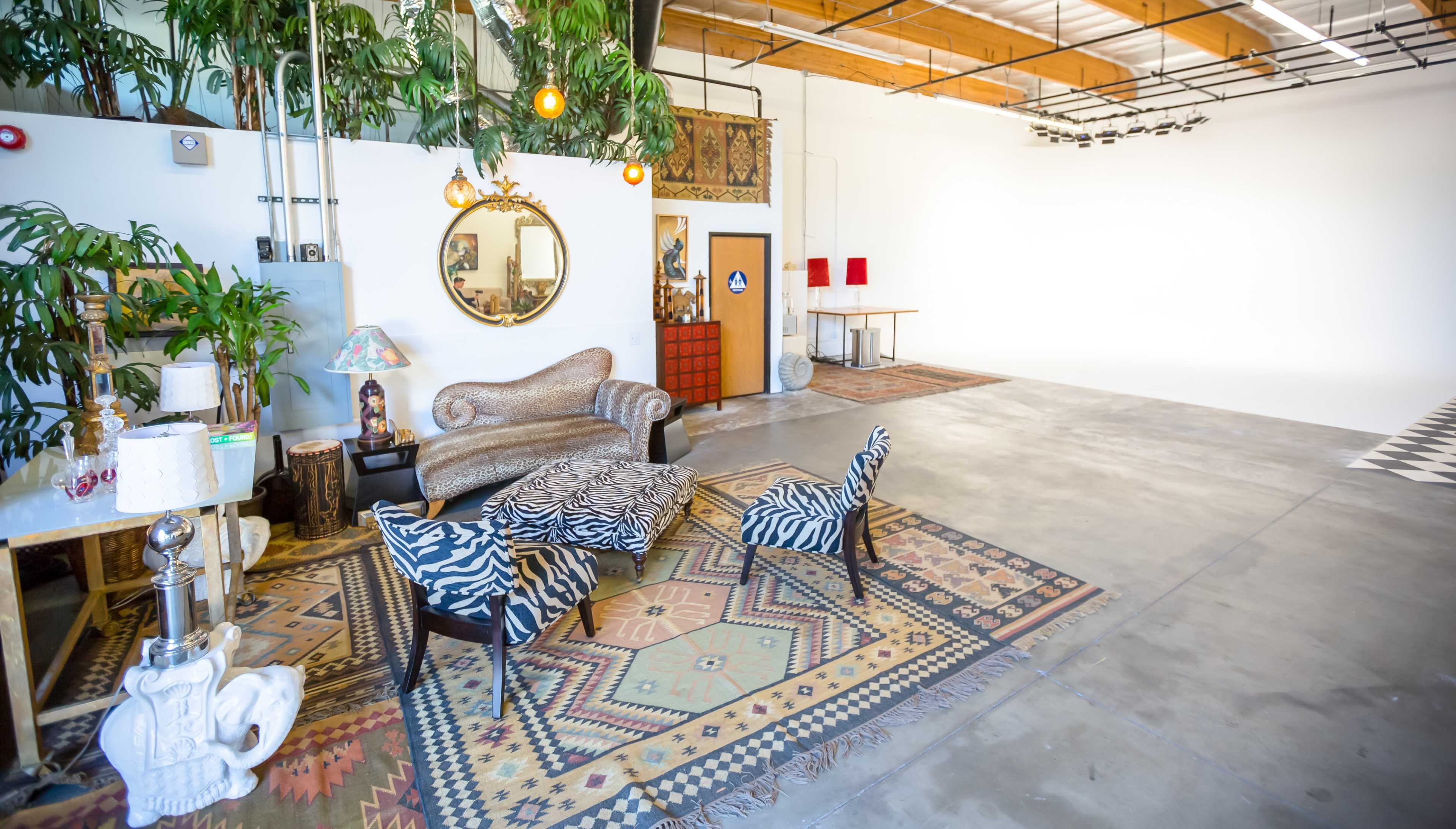 A spacious interior with a patterned rug, a vintage sofa, zebra-print chairs, a decorative mirror, and a large, empty white backdrop area.