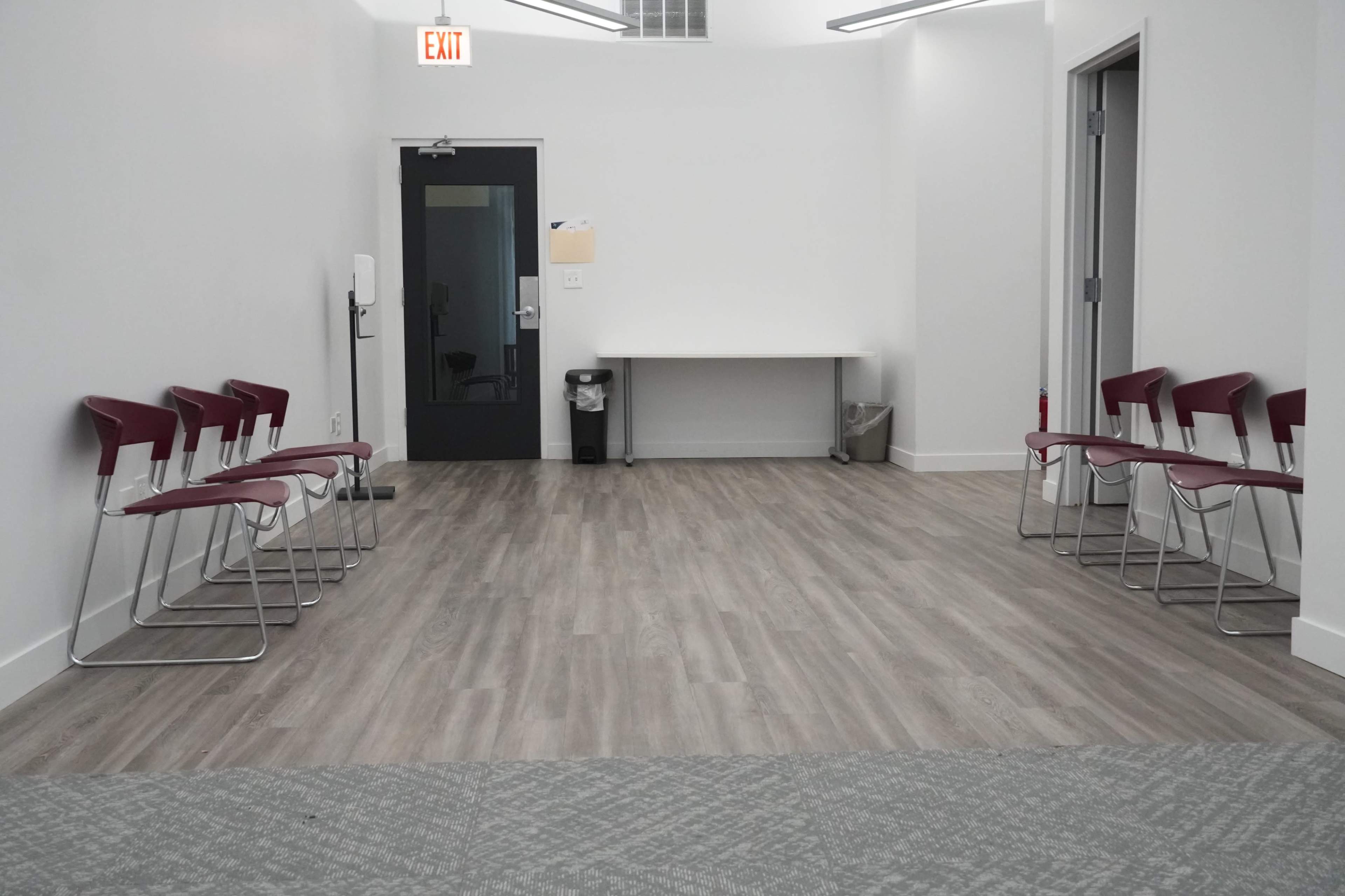 A waiting area features rows of red chairs against a white wall, with a table and trash can in the corner.