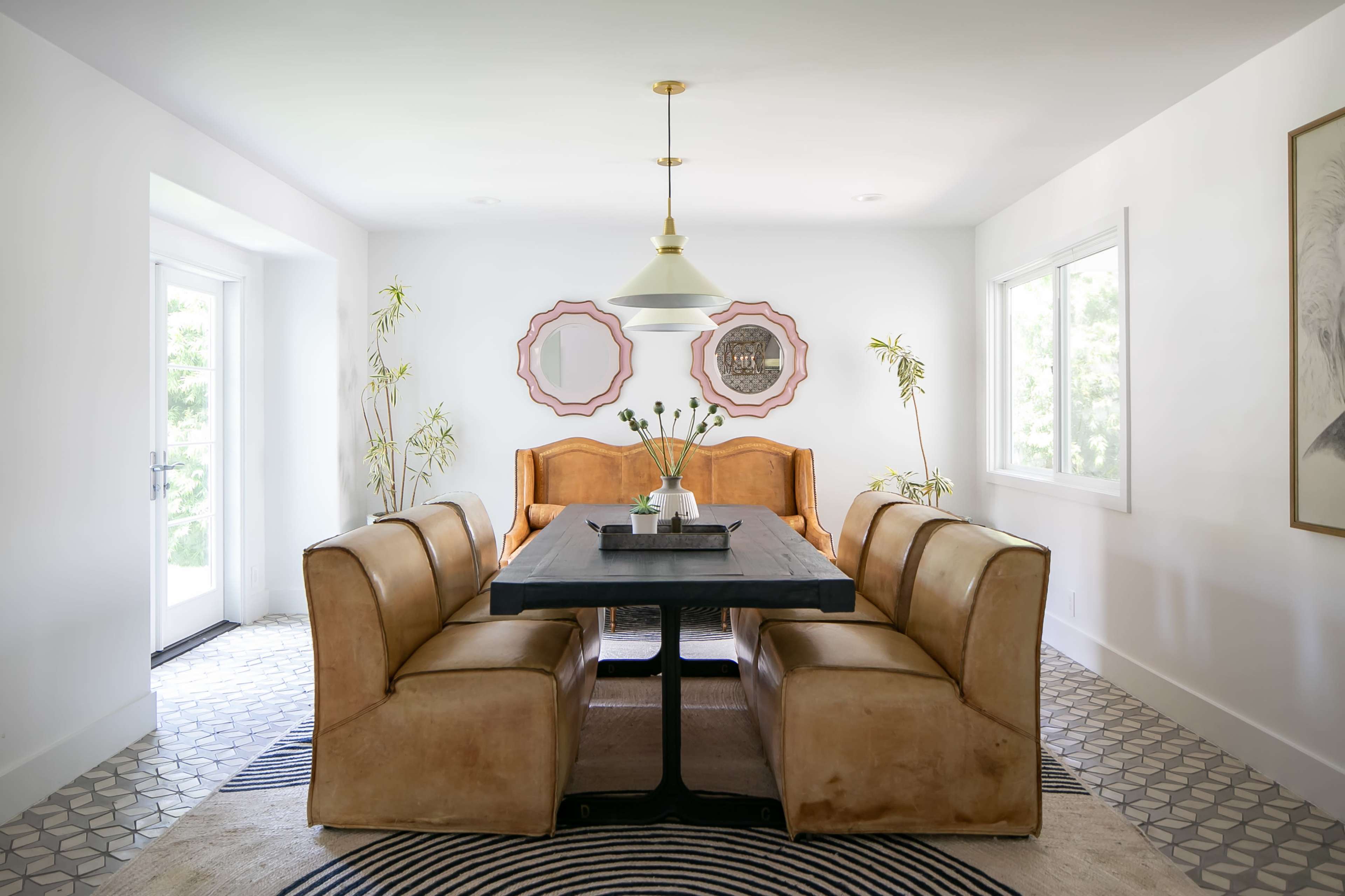 A dining room features a large black table surrounded by leather chairs, with a light fixture above and decorative mirrors on the walls.