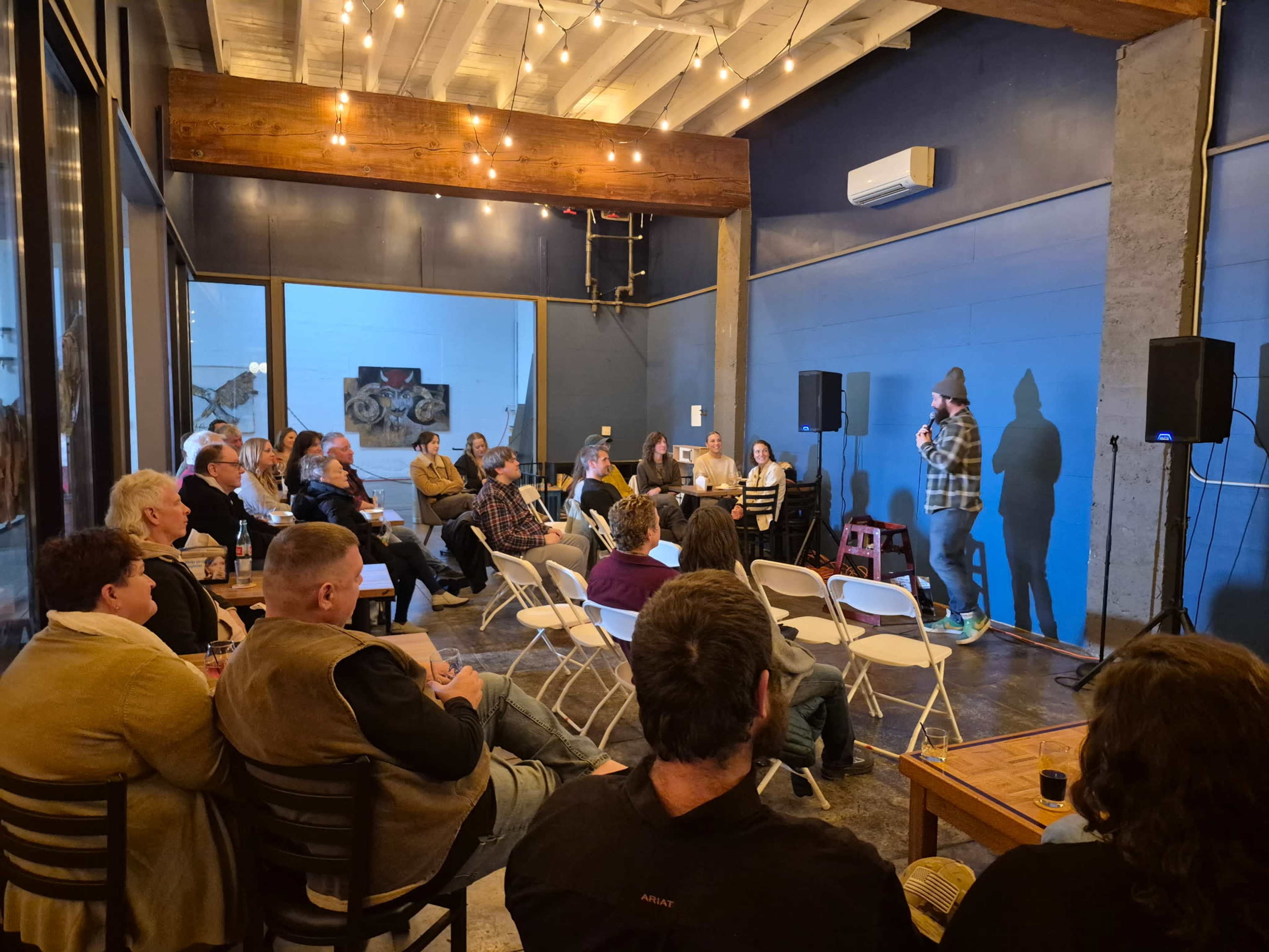 A comedian performs on stage in a crowded venue while an audience watches attentively.