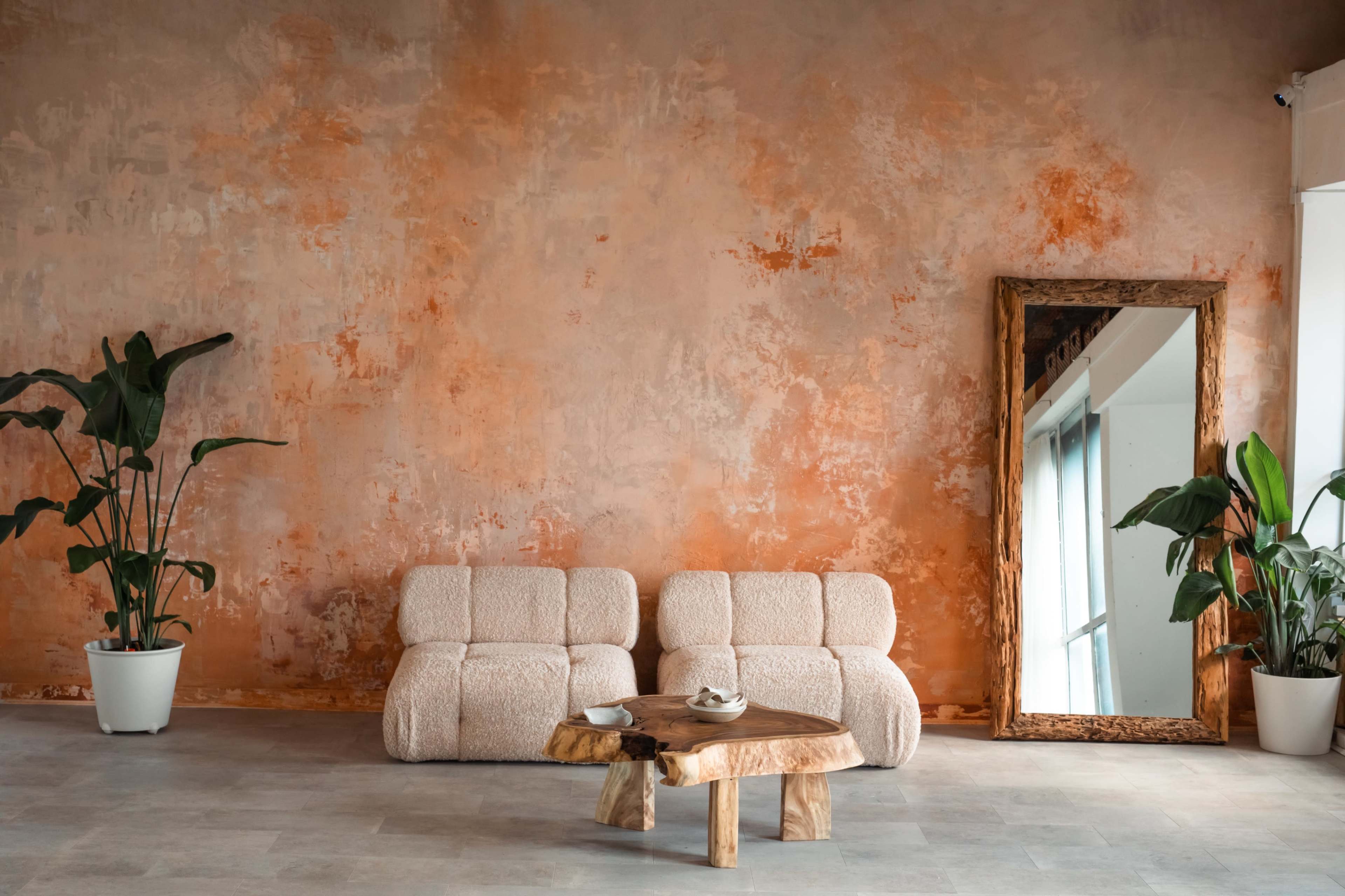 A cozy living space features a textured orange wall, two plush sofas, a wooden coffee table, and decorative plants in white pots.