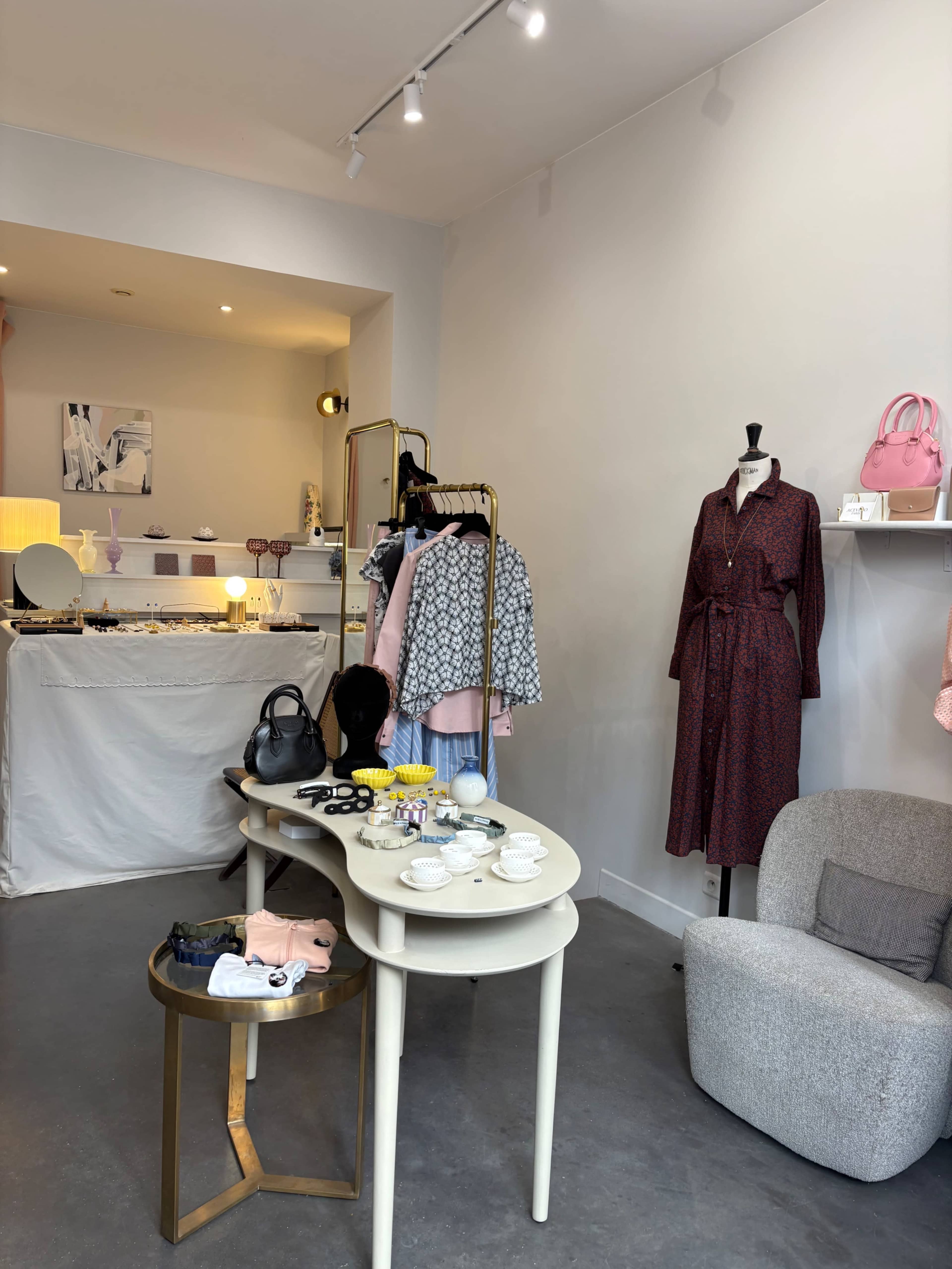 The image shows a boutique interior with clothing racks, a display table featuring accessories, and a cozy seating area.