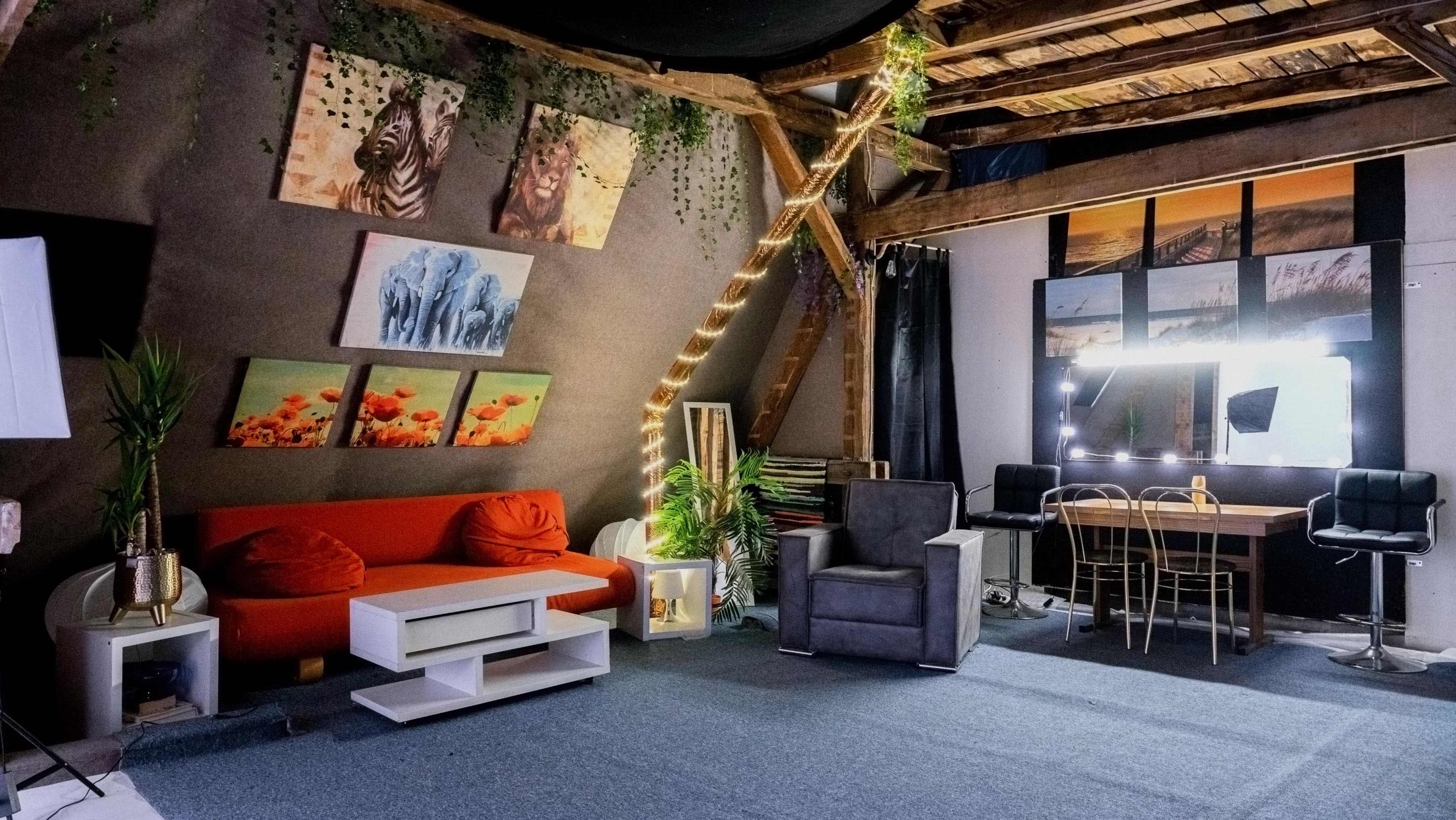 The image depicts a stylish interior space featuring a red sofa, a gray armchair, a dining table with chairs, and framed artwork on the walls, all arranged under wooden beams and soft lighting.