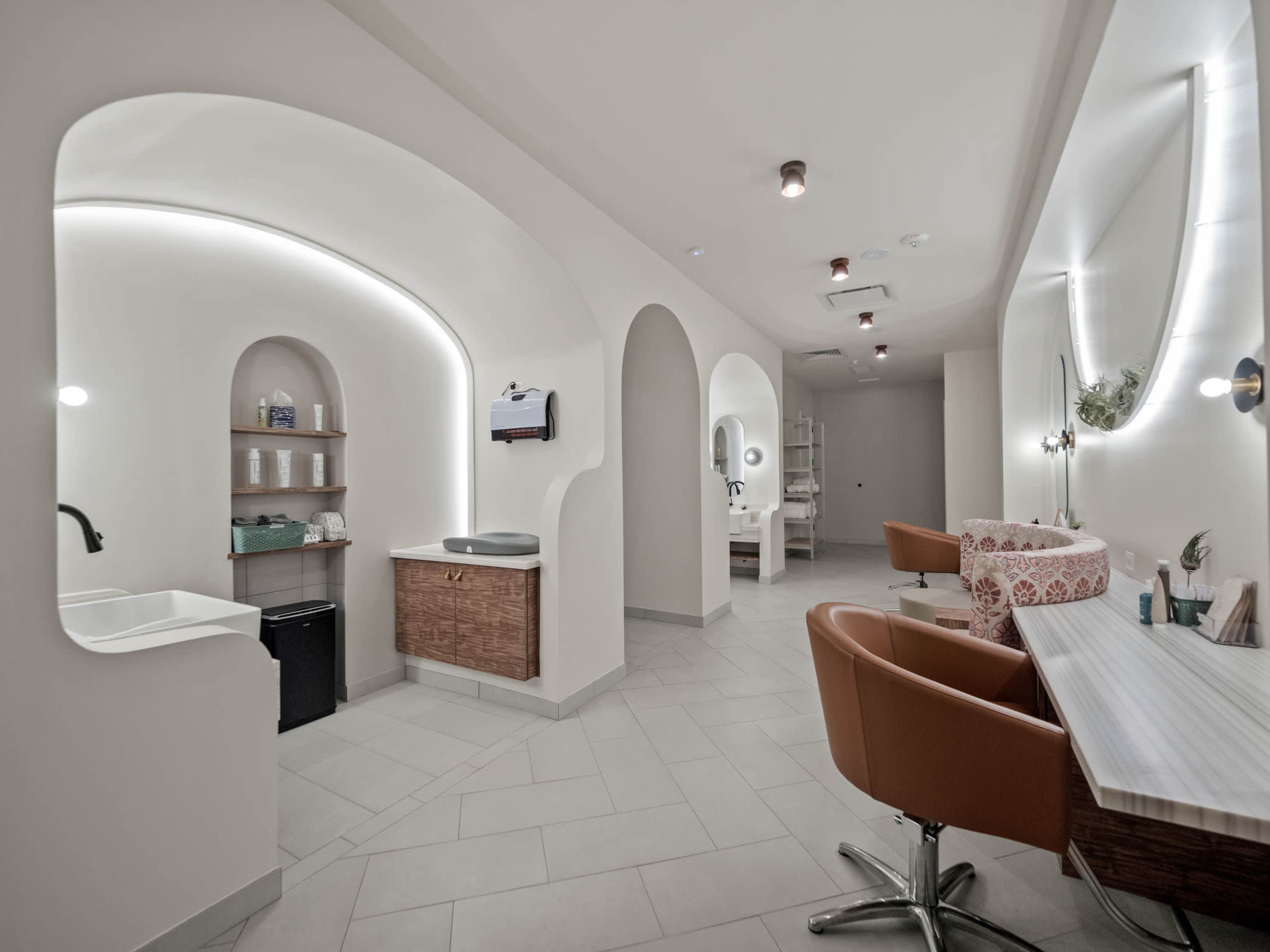 The image shows a modern salon interior with arched designs, featuring a work station, a wash area, and organized storage spaces.