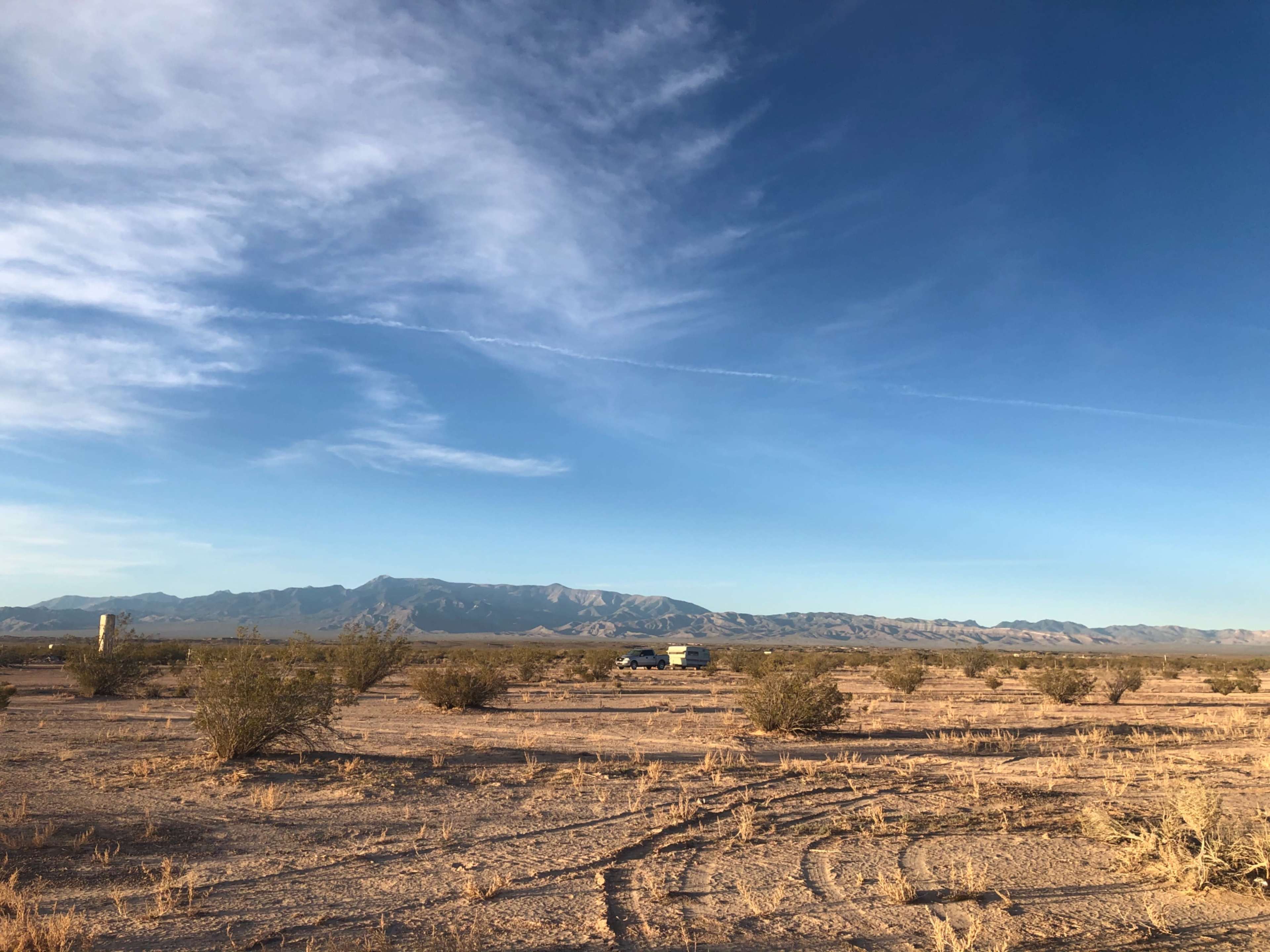 A vast desert landscape with sparse vegetation and distant mountains under a clear blue sky.