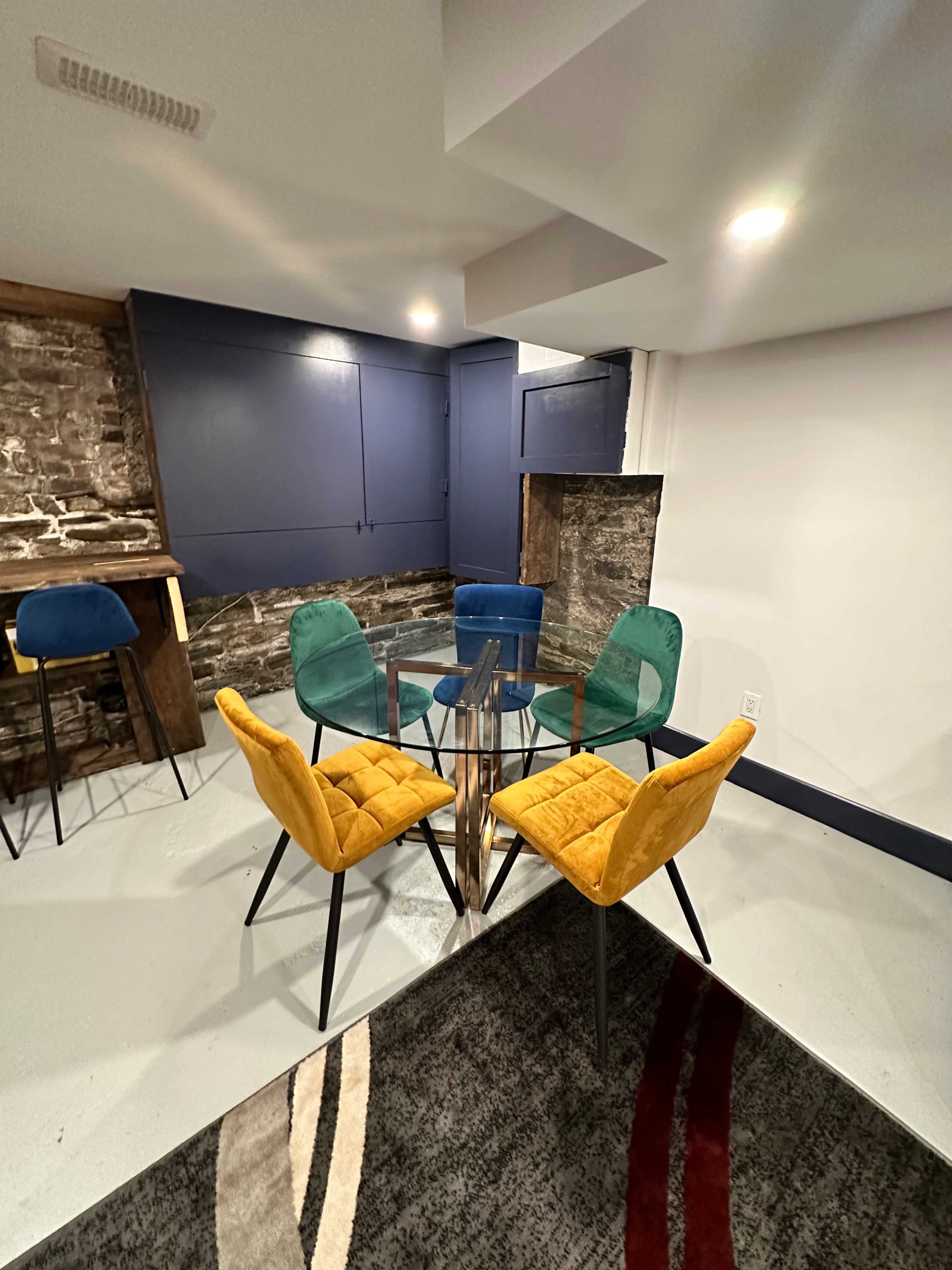 A modern seating area features a glass table surrounded by four colorful chairs on a patterned rug.