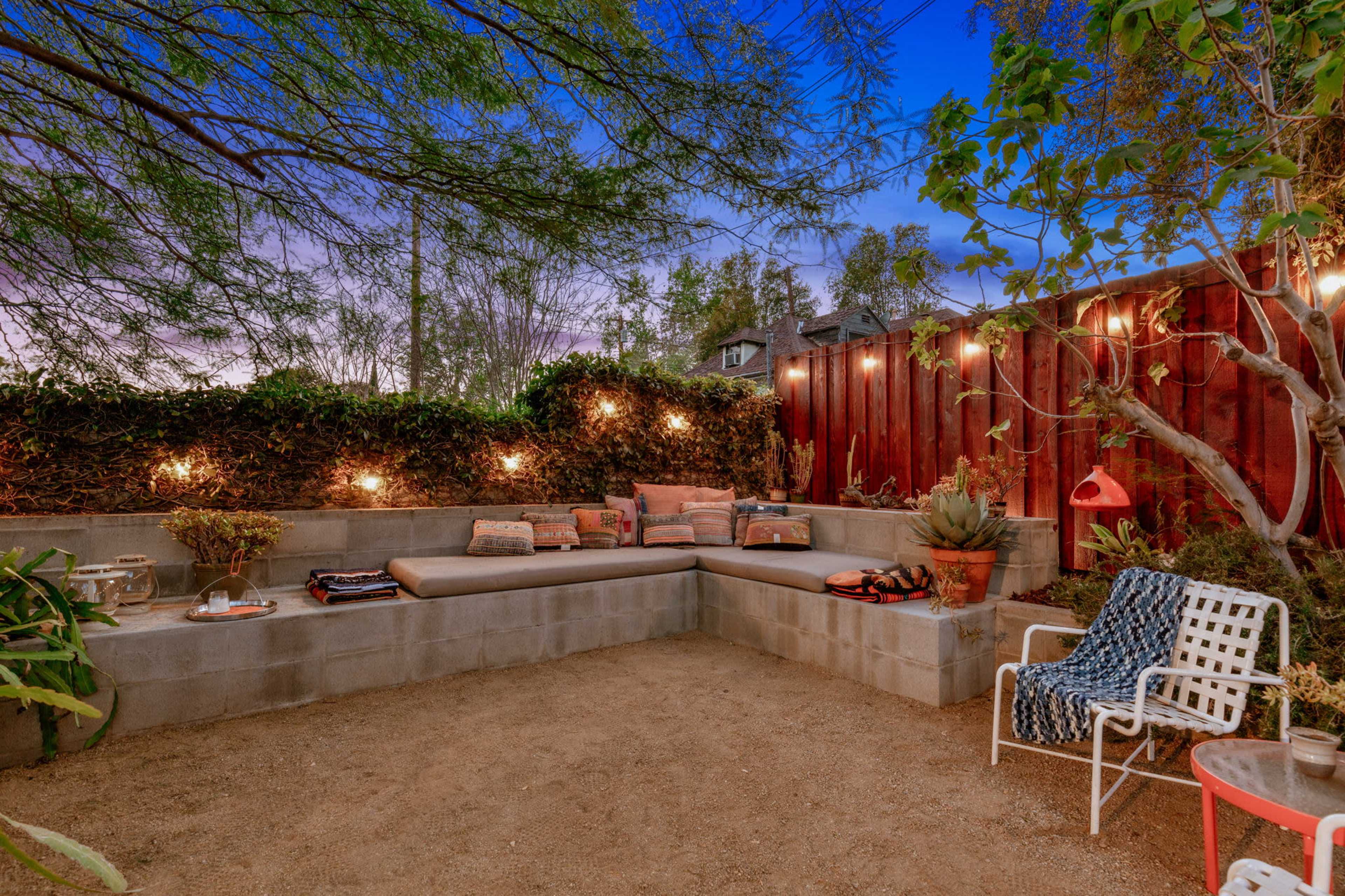 A cozy outdoor seating area with a concrete wall bench, string lights, and various plants in a gravel landscape.