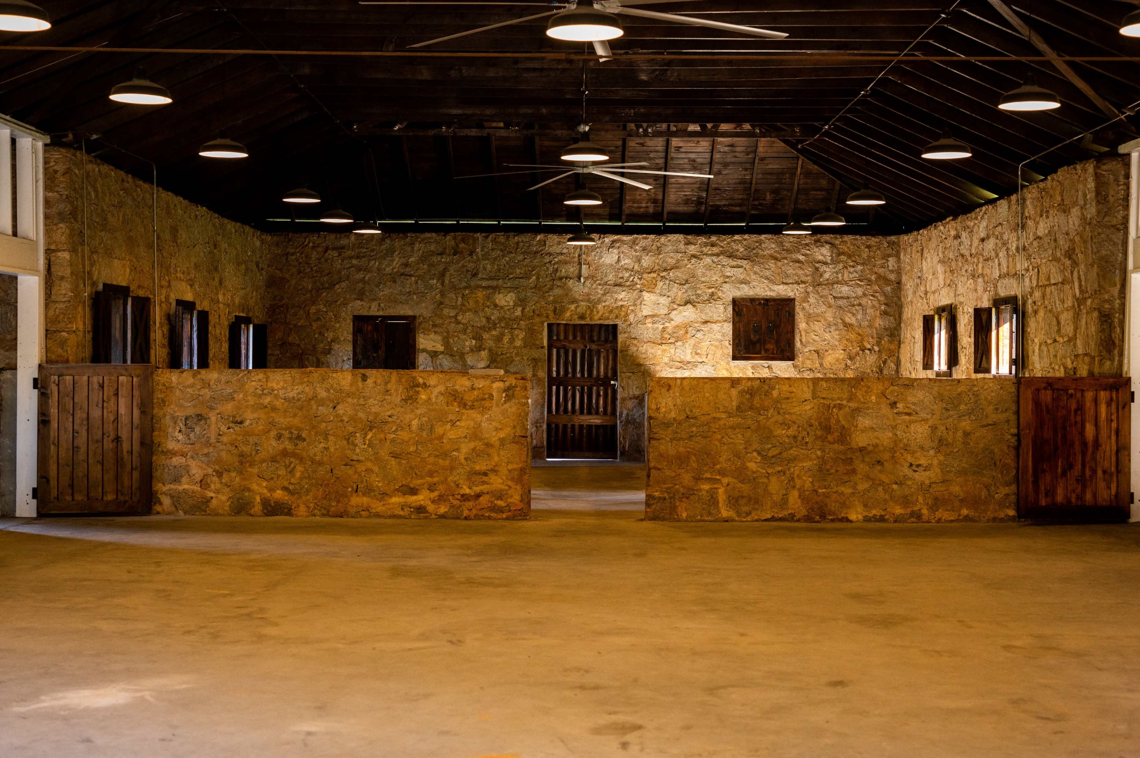 The image shows a spacious interior with stone walls, wooden doors, and several ceiling fans, creating an open area.
