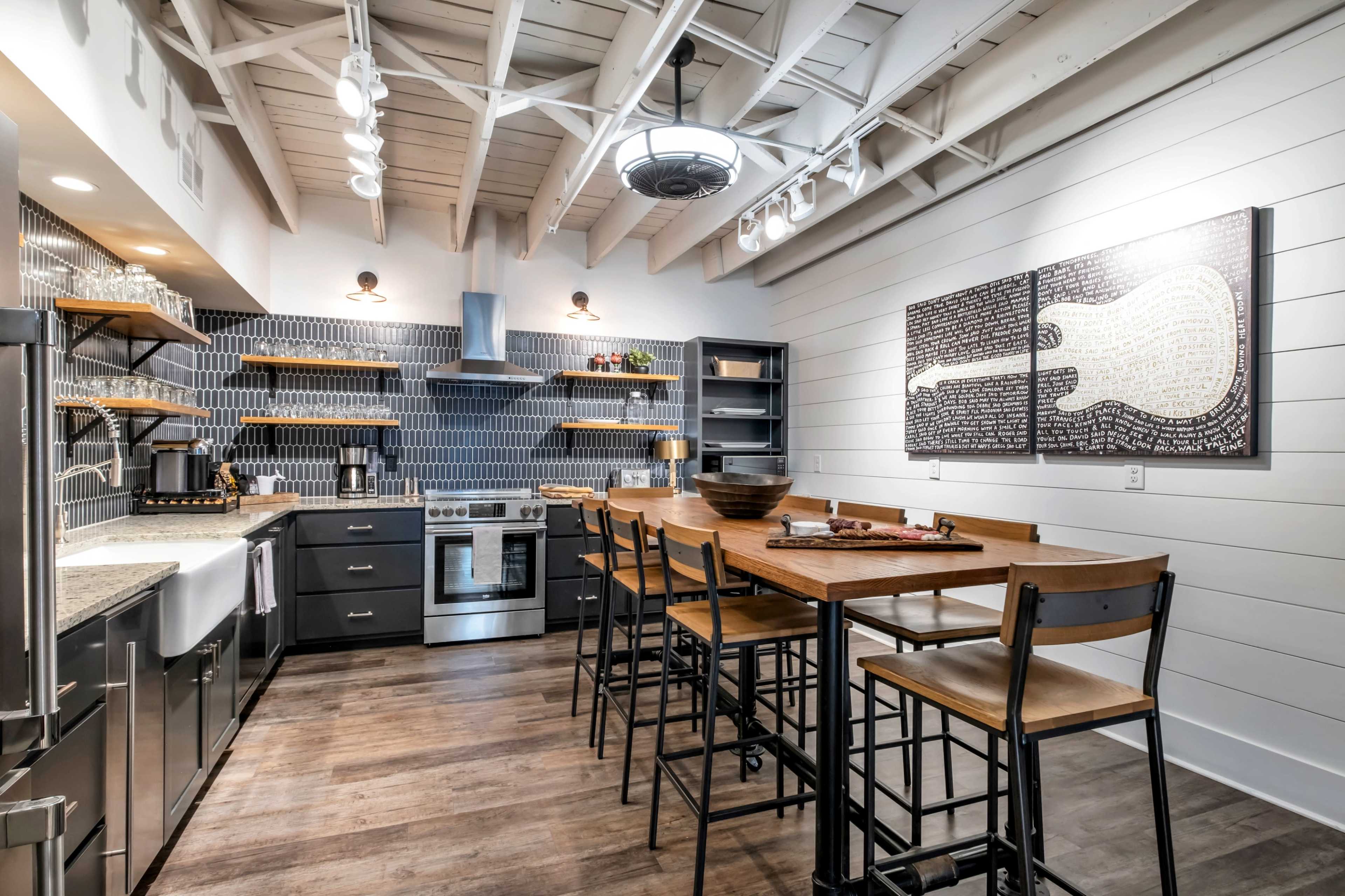 The image shows a modern kitchen featuring a large wooden island with bar stools, stainless steel appliances, and blue tile backsplash.