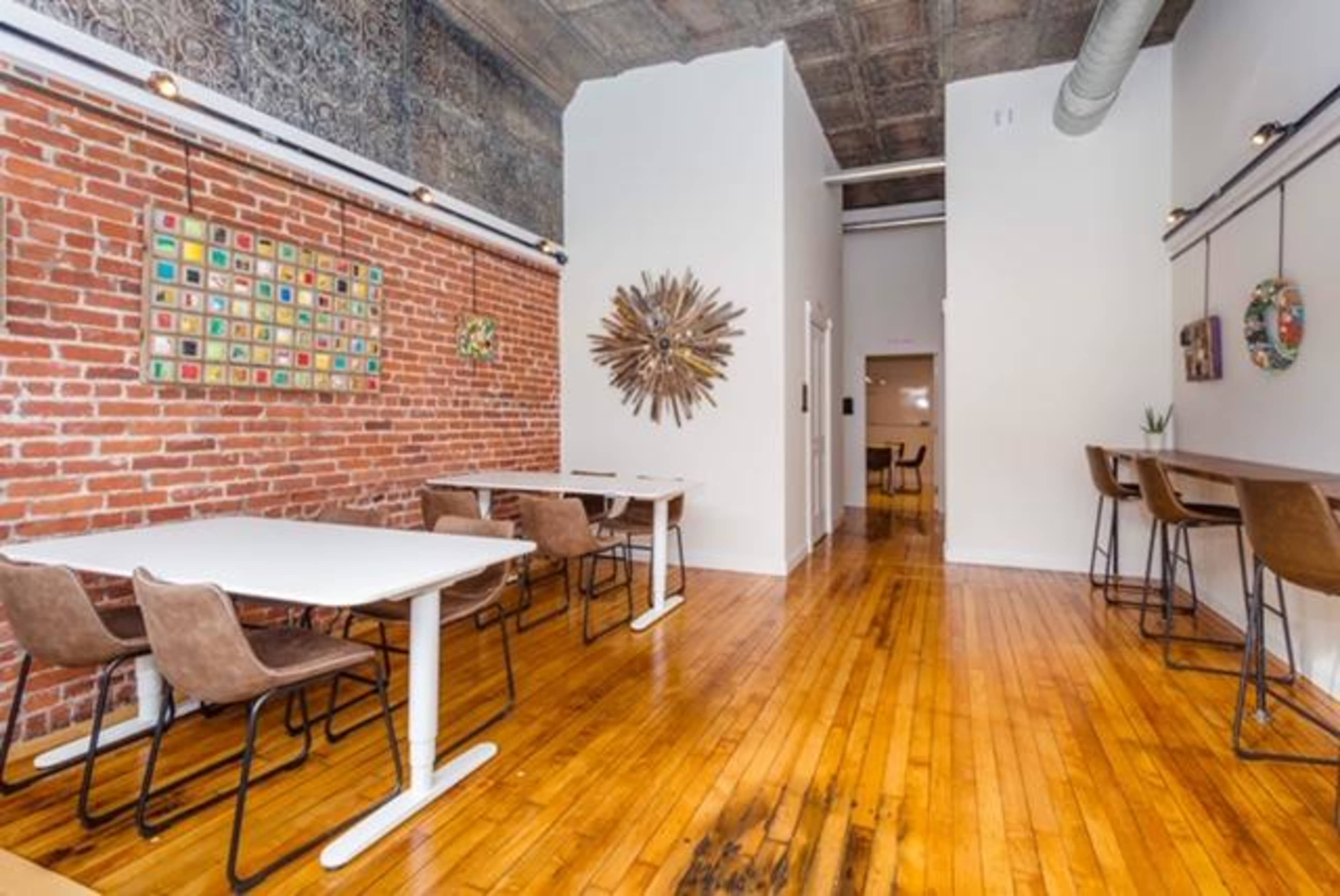 A bright, open space with wooden floors, exposed brick walls, and several tables arranged for seating.