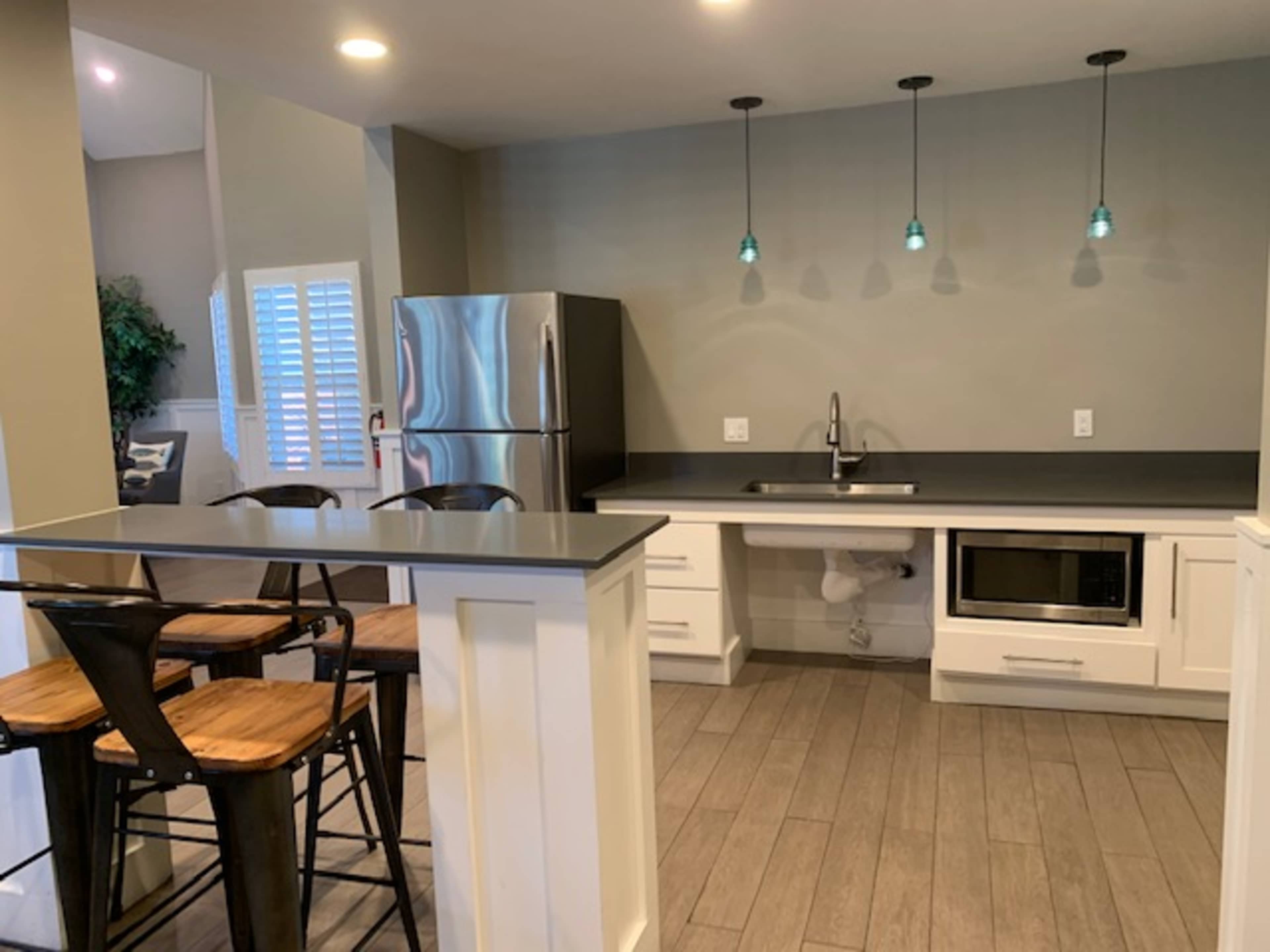 A modern kitchen with stainless steel appliances, a gray countertop, bar seating, and pendant lights above the sink.