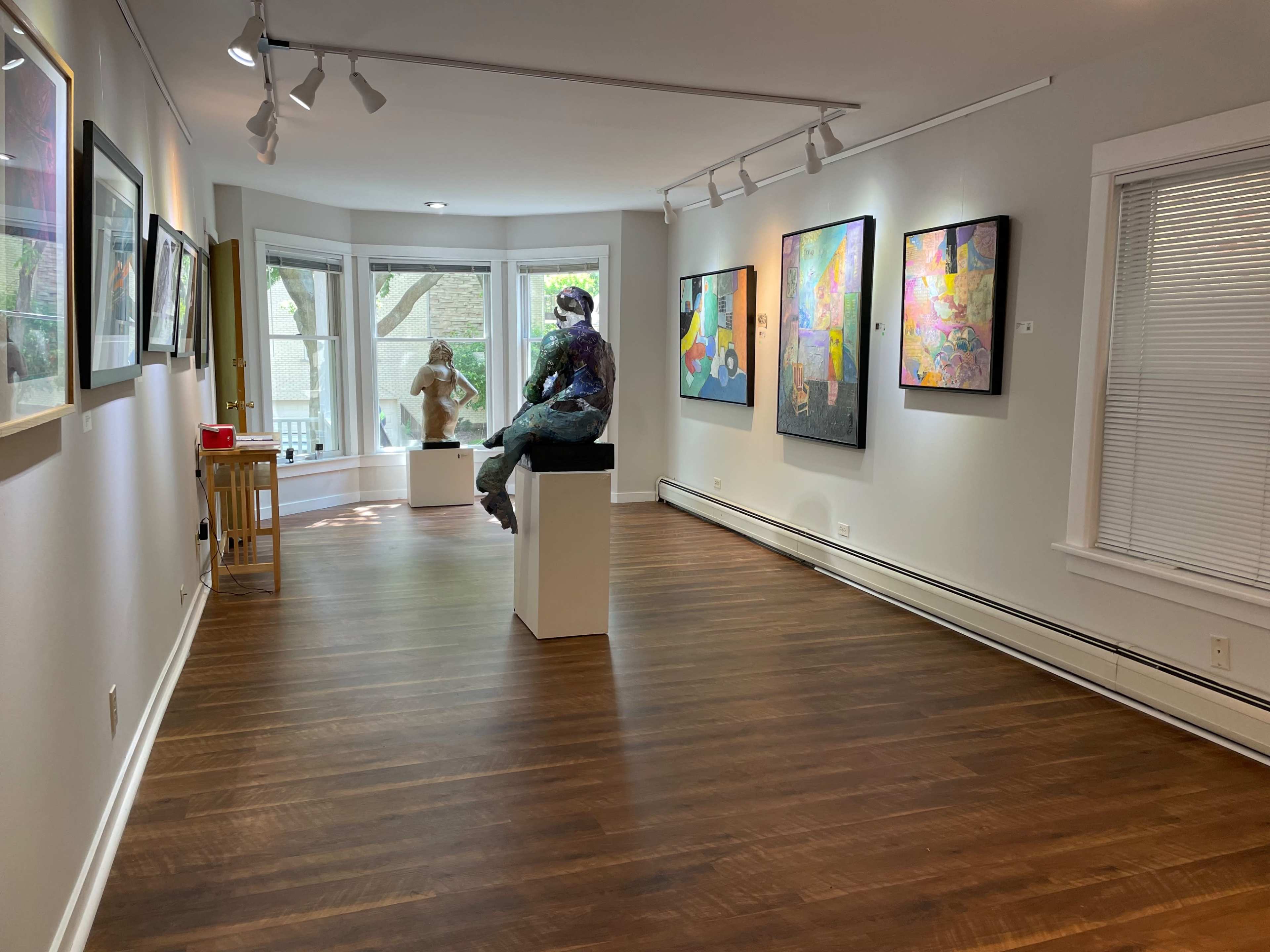 An art gallery featuring a sculpture on a pedestal and various colorful paintings hanging on the white walls.