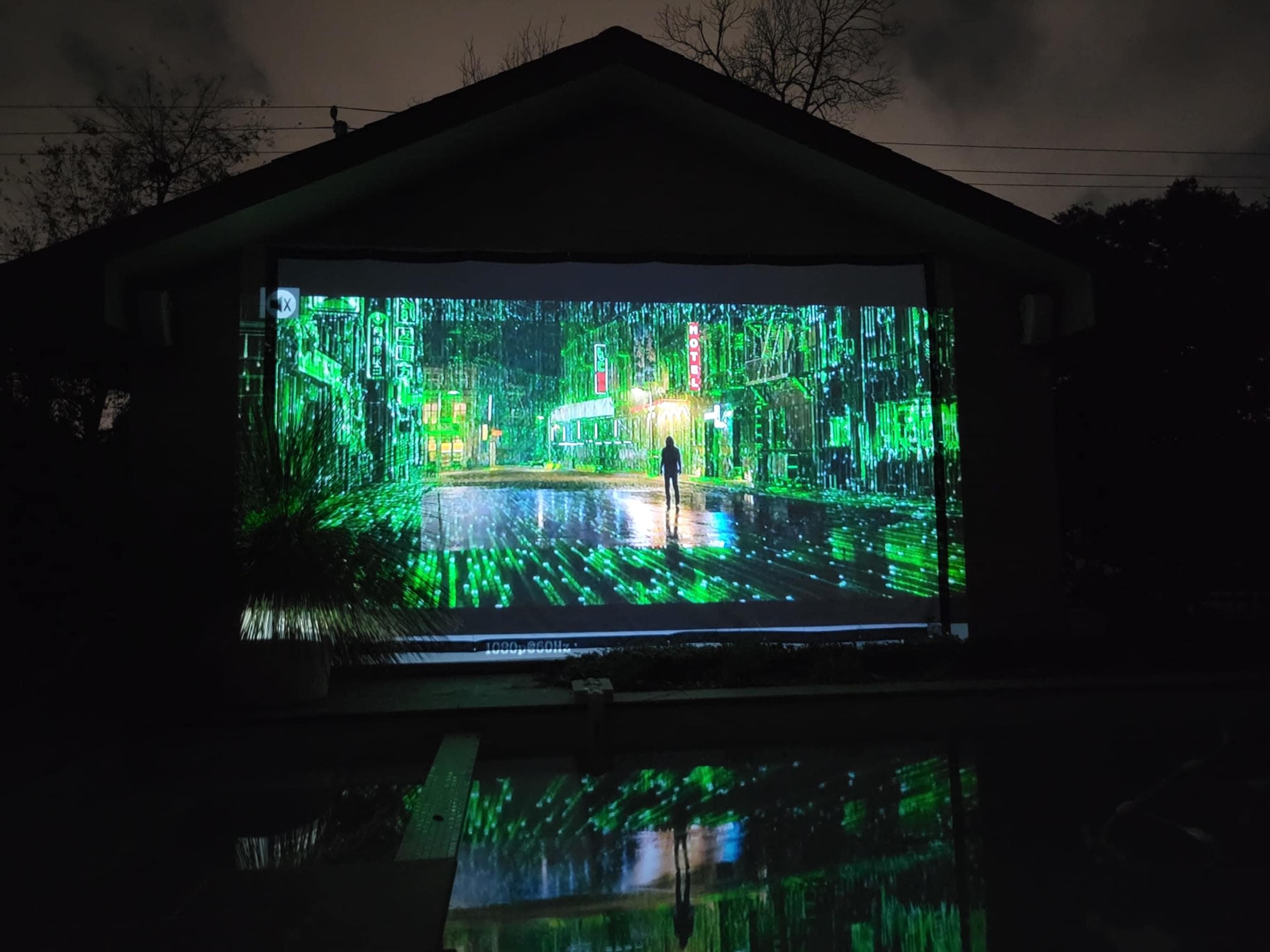A large projection on a building's wall depicts a vibrant city street scene illuminated in green tones.