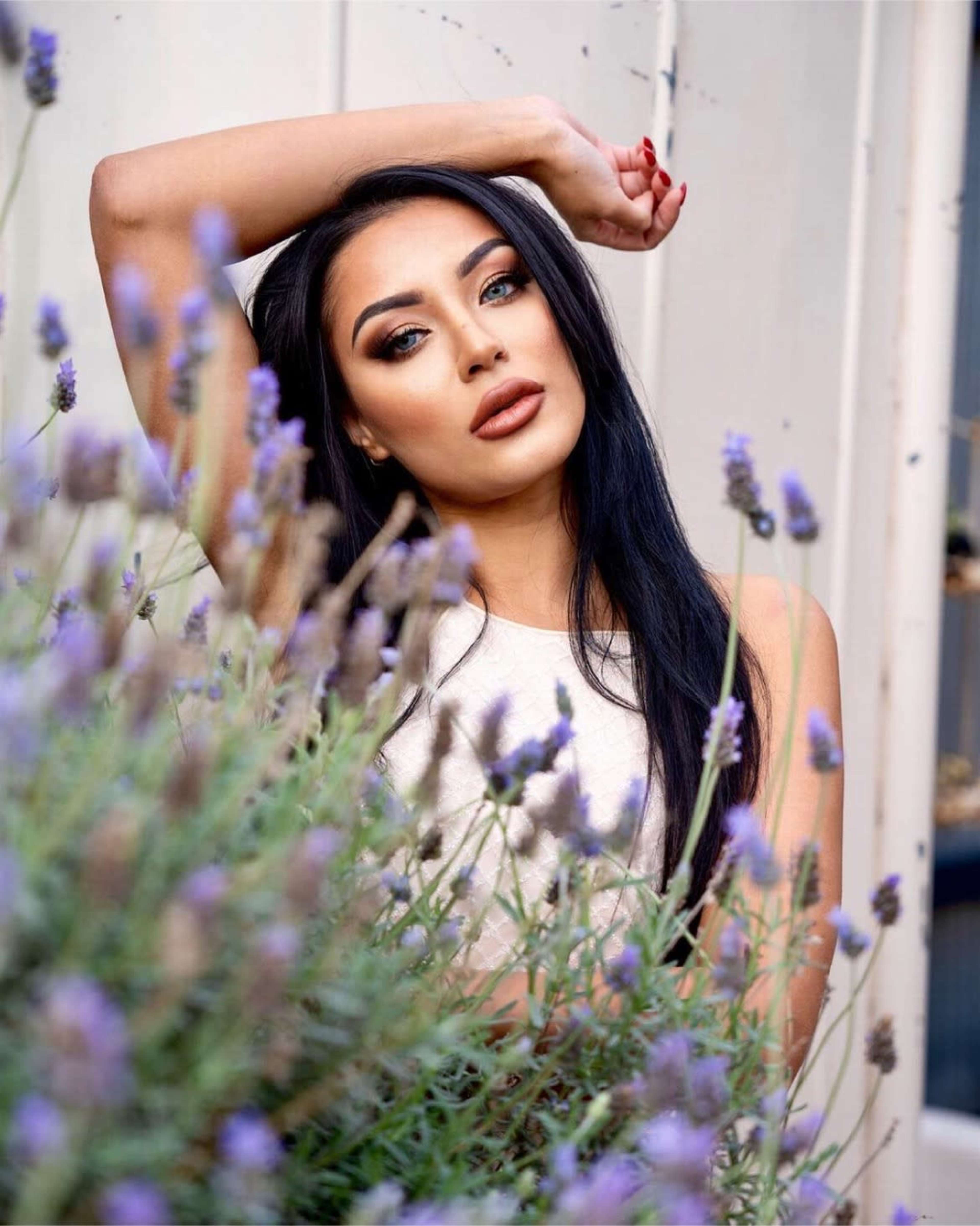 A woman poses with one arm raised while surrounded by lavender plants.