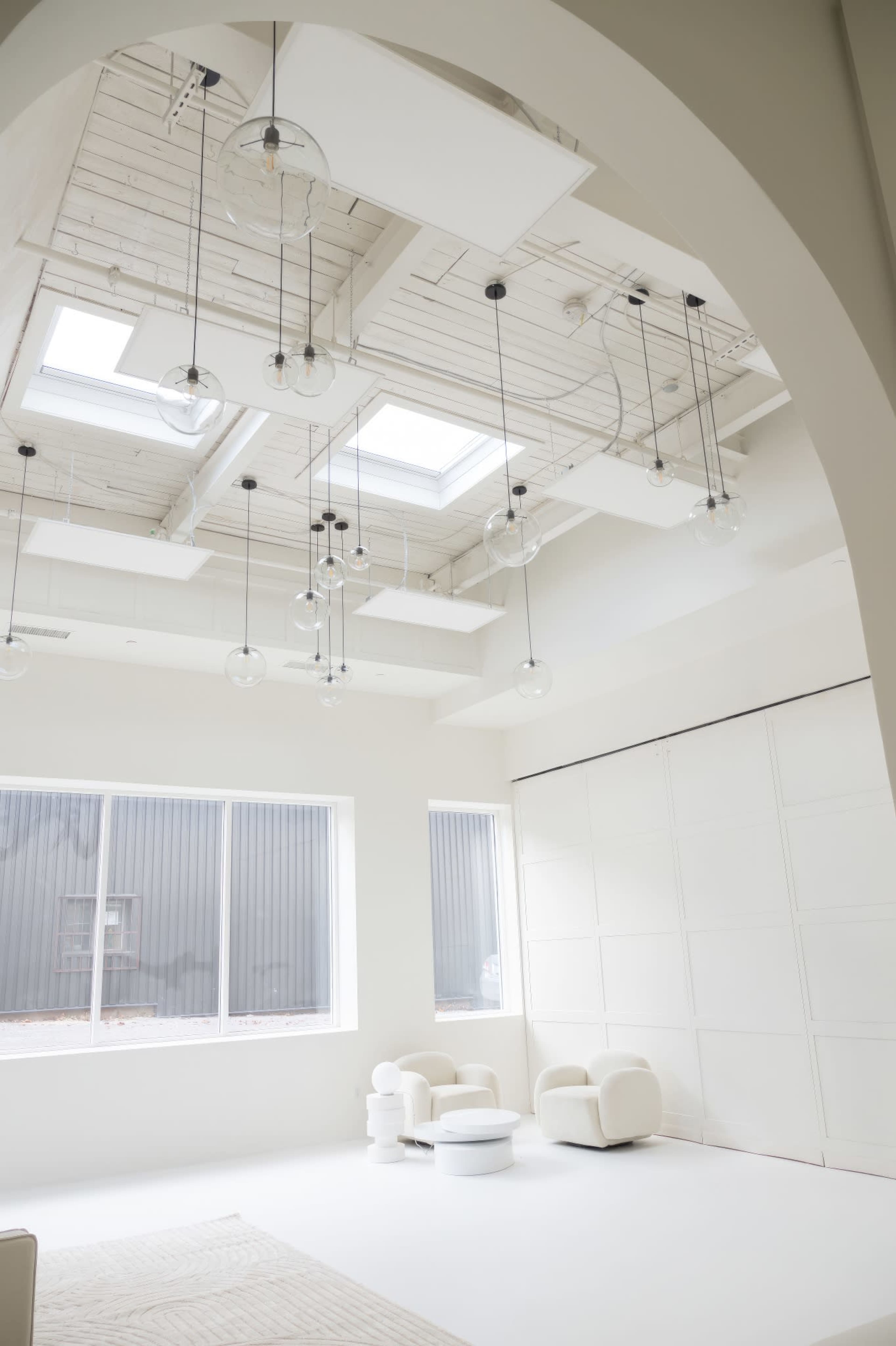 A modern, minimalist interior space with white walls, large windows, and circular pendant lights hanging from the ceiling.