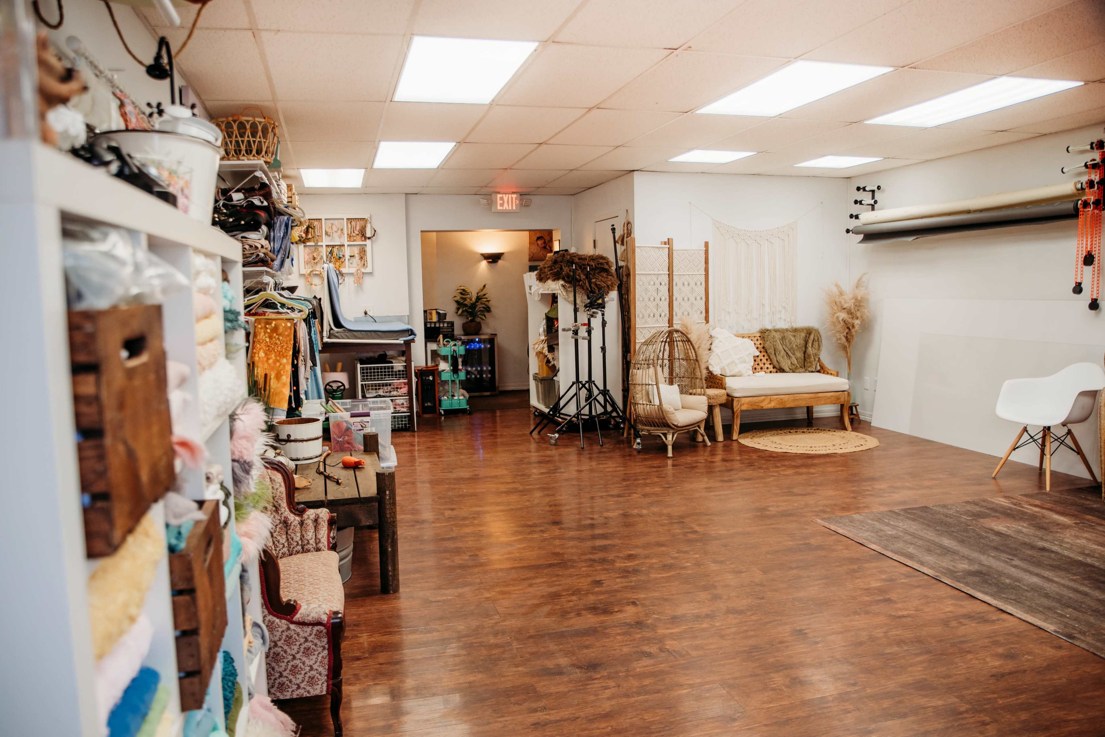 A spacious, well-lit studio with a variety of props and furniture, including a seating area and storage shelves along the walls.
