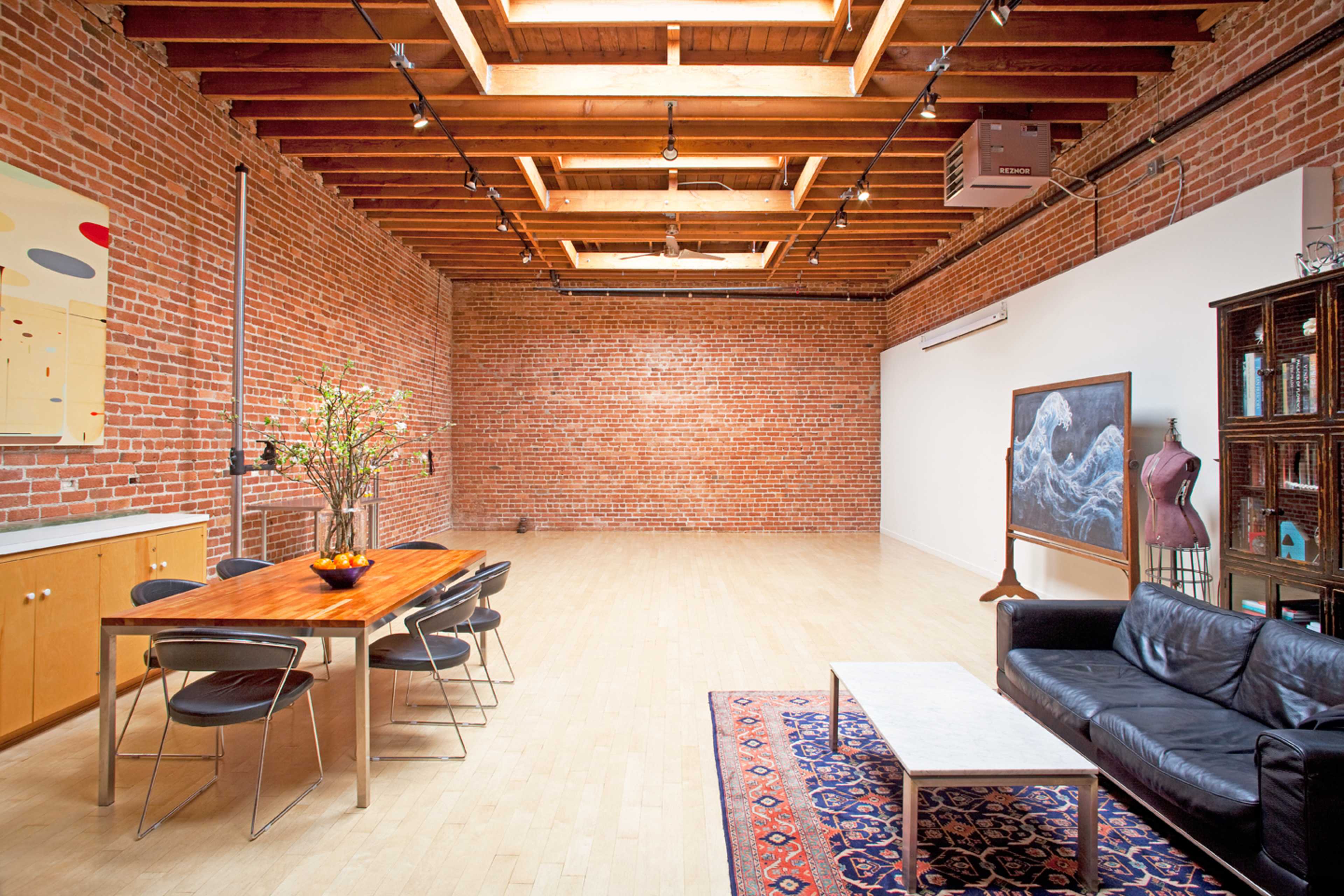 A spacious interior with exposed brick walls, wooden beams, a dining table with chairs, a black leather sofa, and decorative furniture.