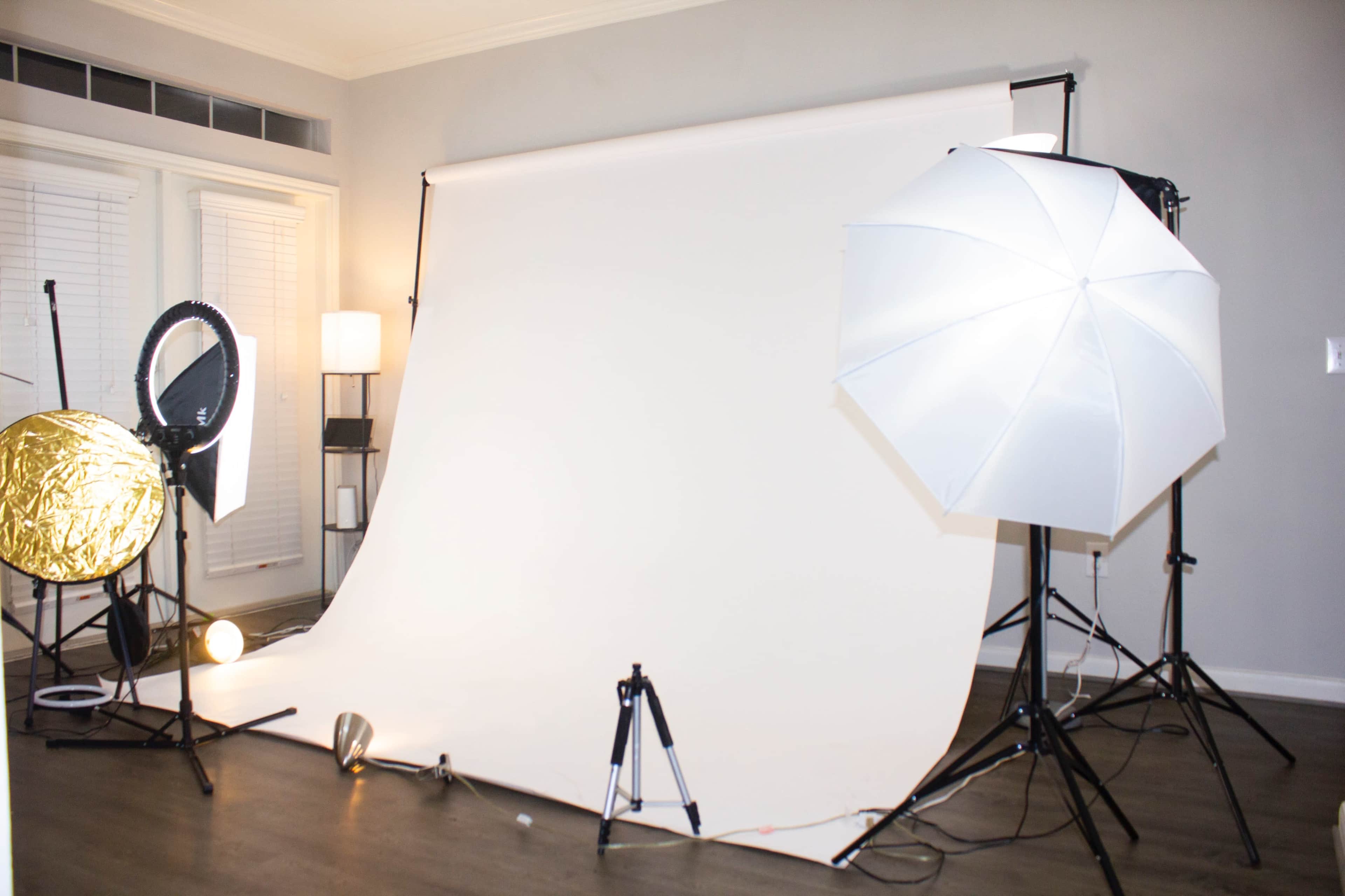 A photography studio setup with a white backdrop and various lighting equipment, including softboxes and reflectors.