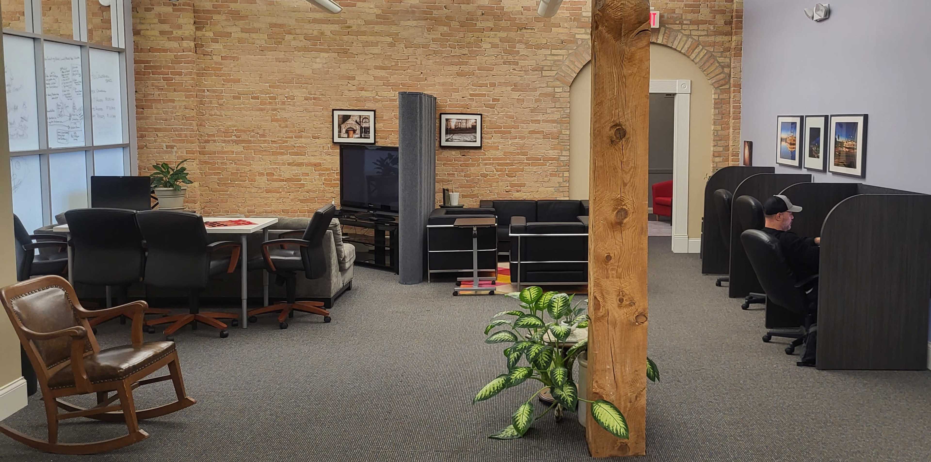 A modern office space with brick walls, a television, desks, chairs, and a potted plant.