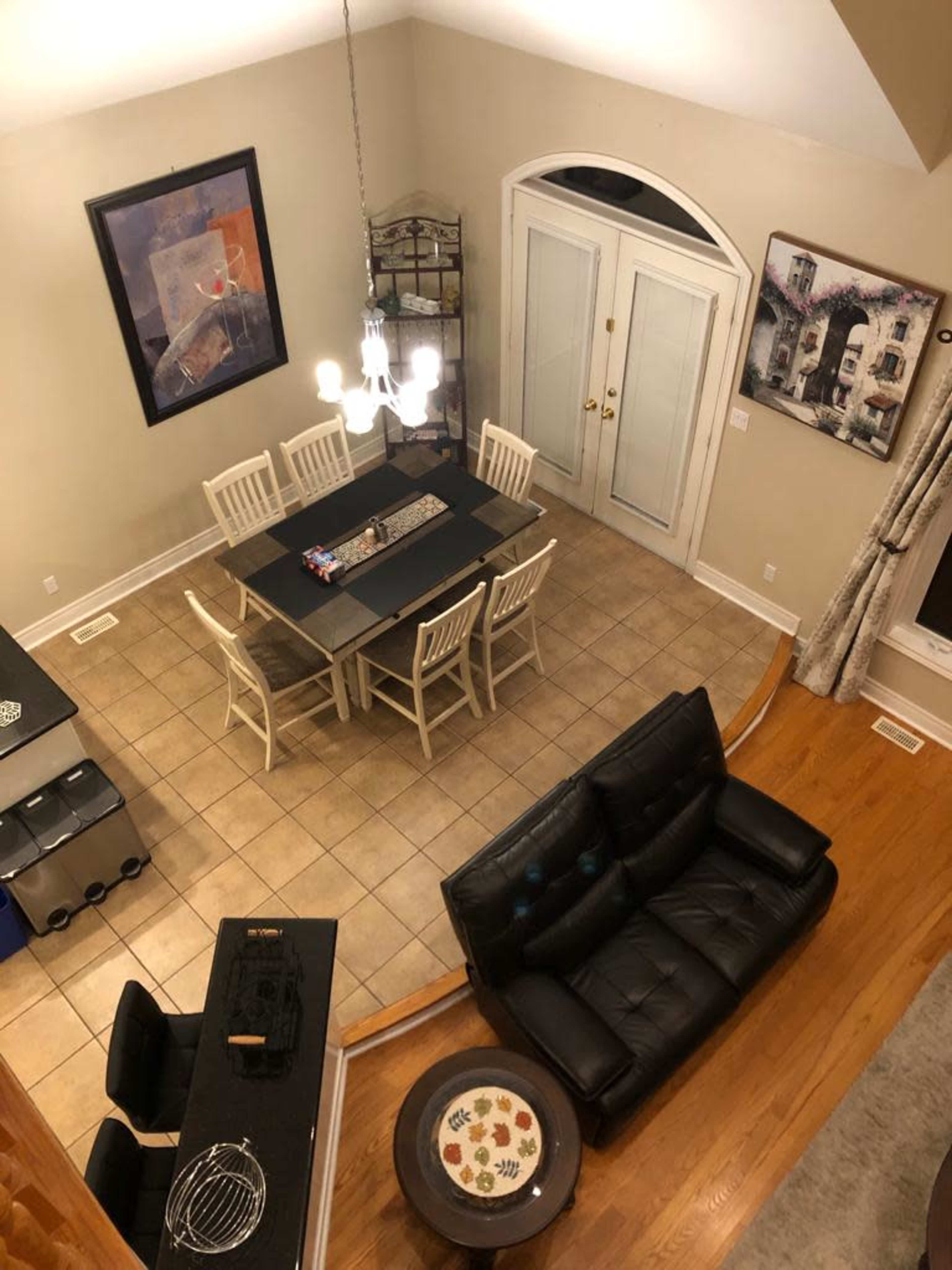 An overhead view of a dining area with a table set for six chairs, a black leather sofa, and a tiled floor.