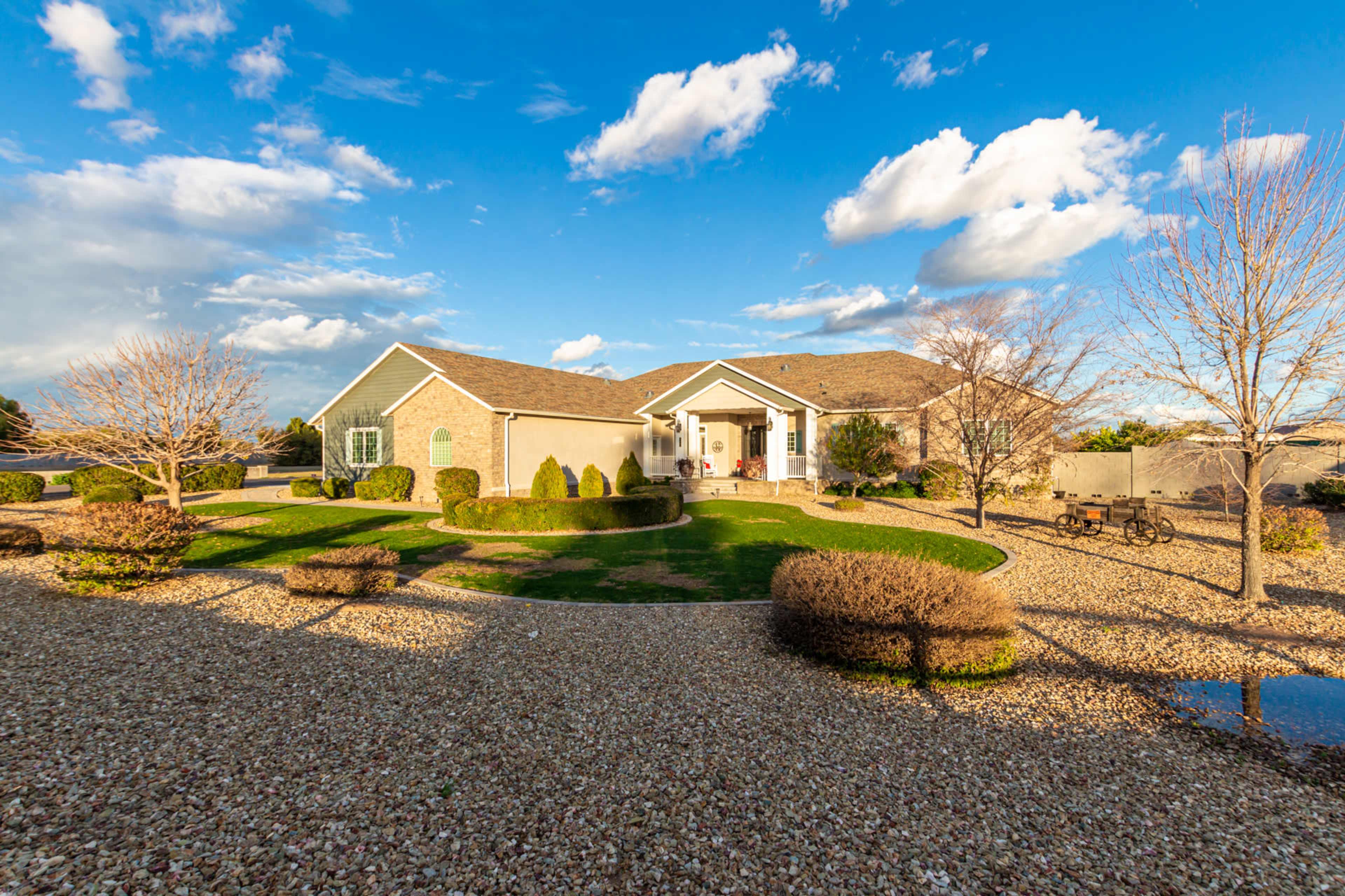 A well-landscaped home features a large front yard with gravel pathways, trimmed bushes, and a porch under partly cloudy skies.